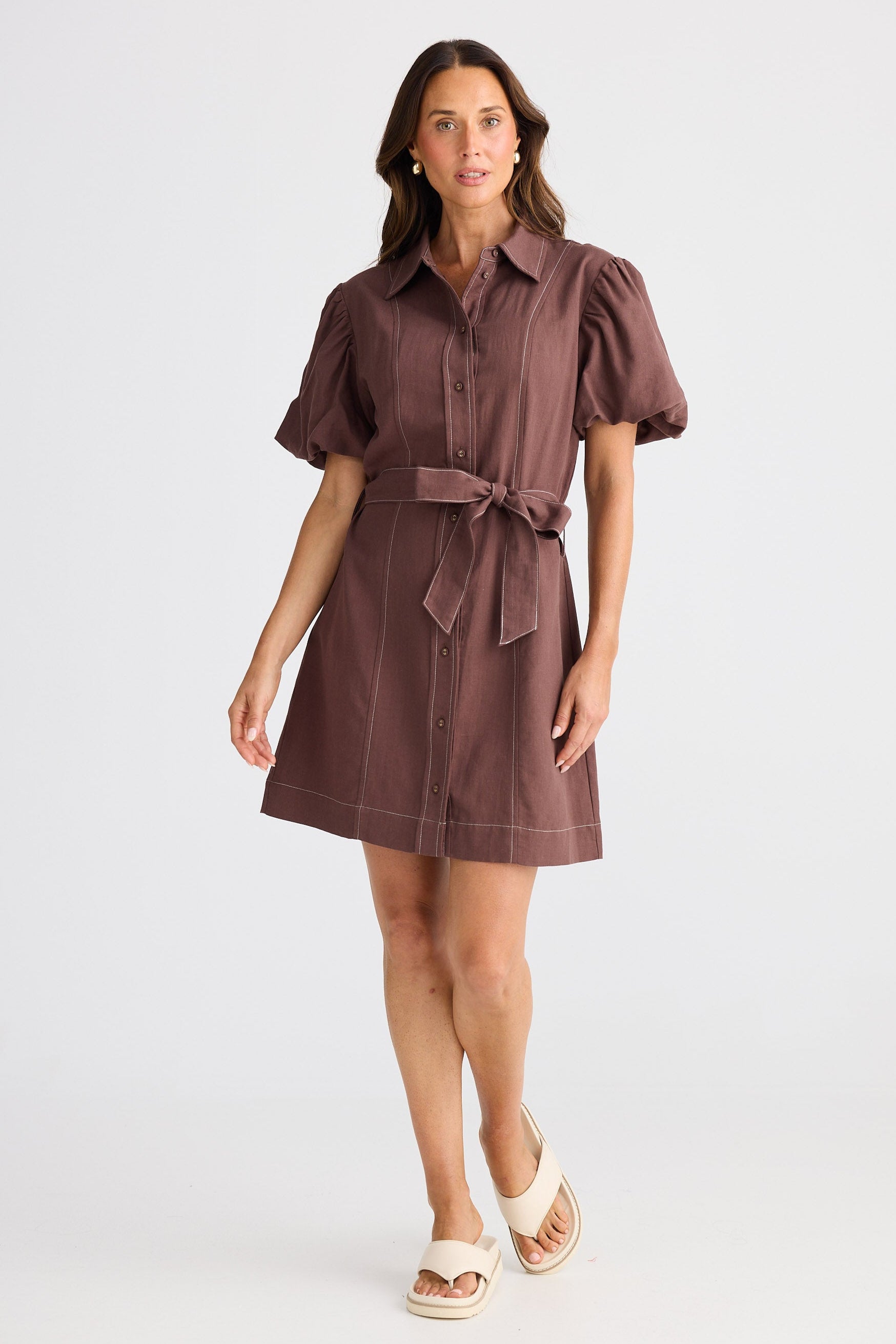 Woman wearing a brown dress with puff sleeves on a white background
