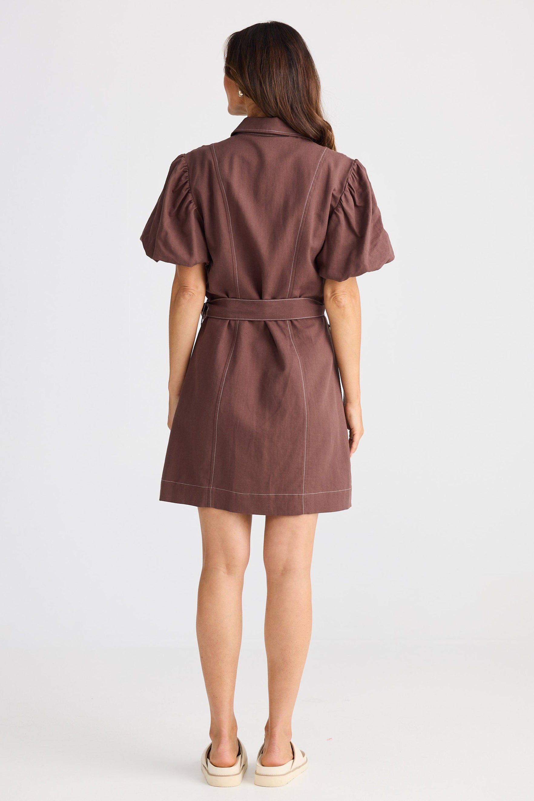 Woman wearing a brown dress with puff sleeves on a white background