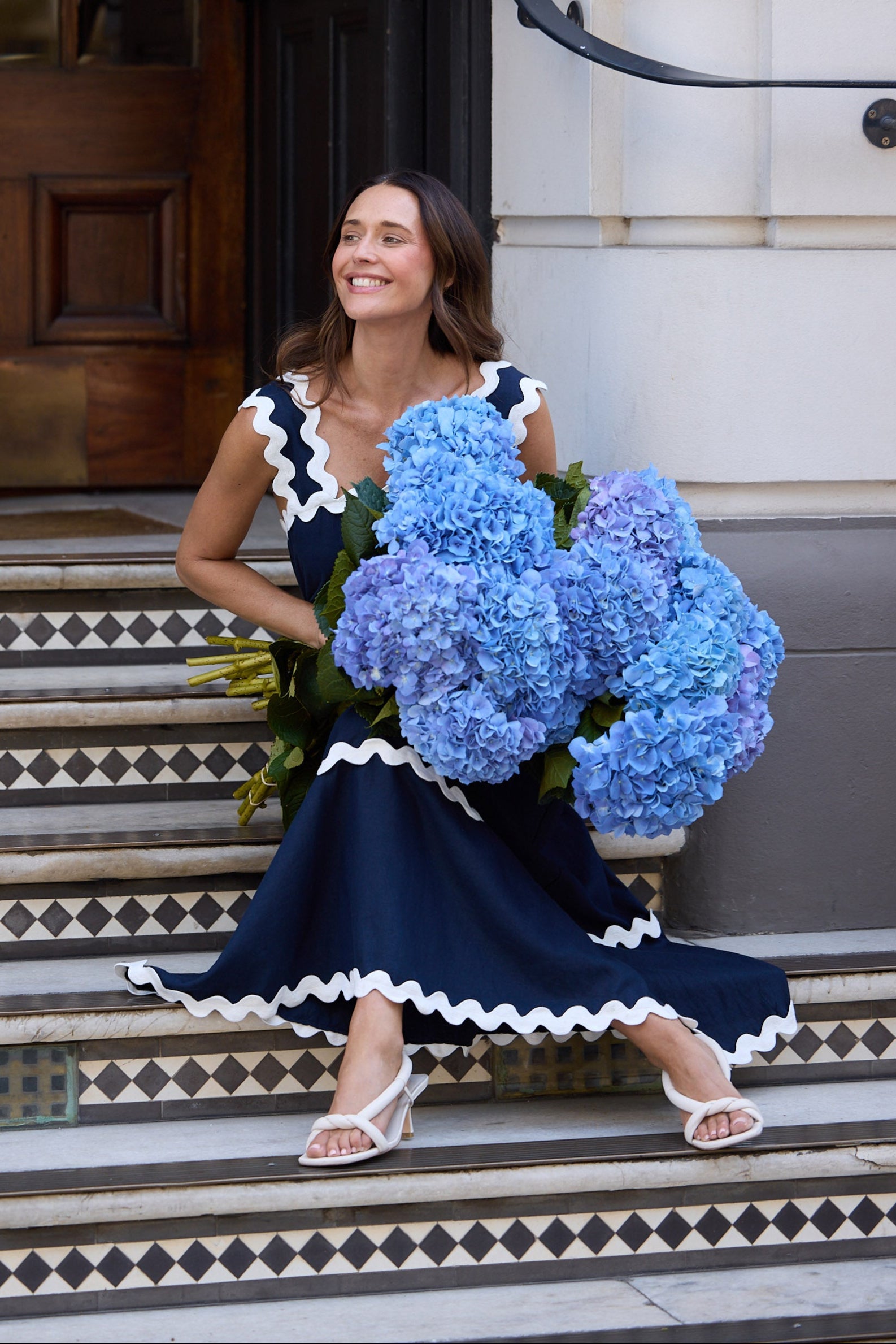 Woman in a navy dress holding blue flowers on steps outside a building