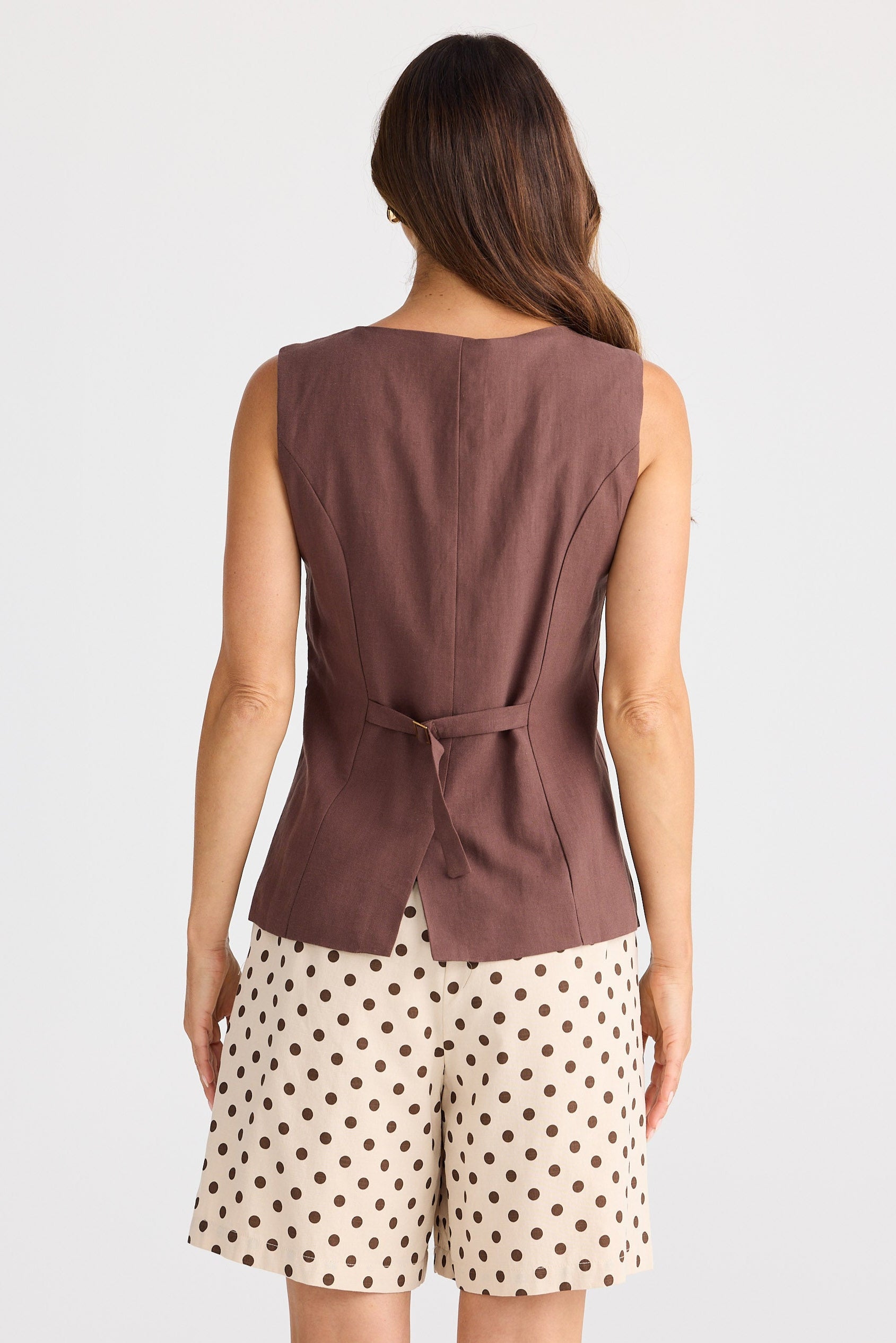 Woman wearing a brown sleeveless top and patterned shorts on a white background