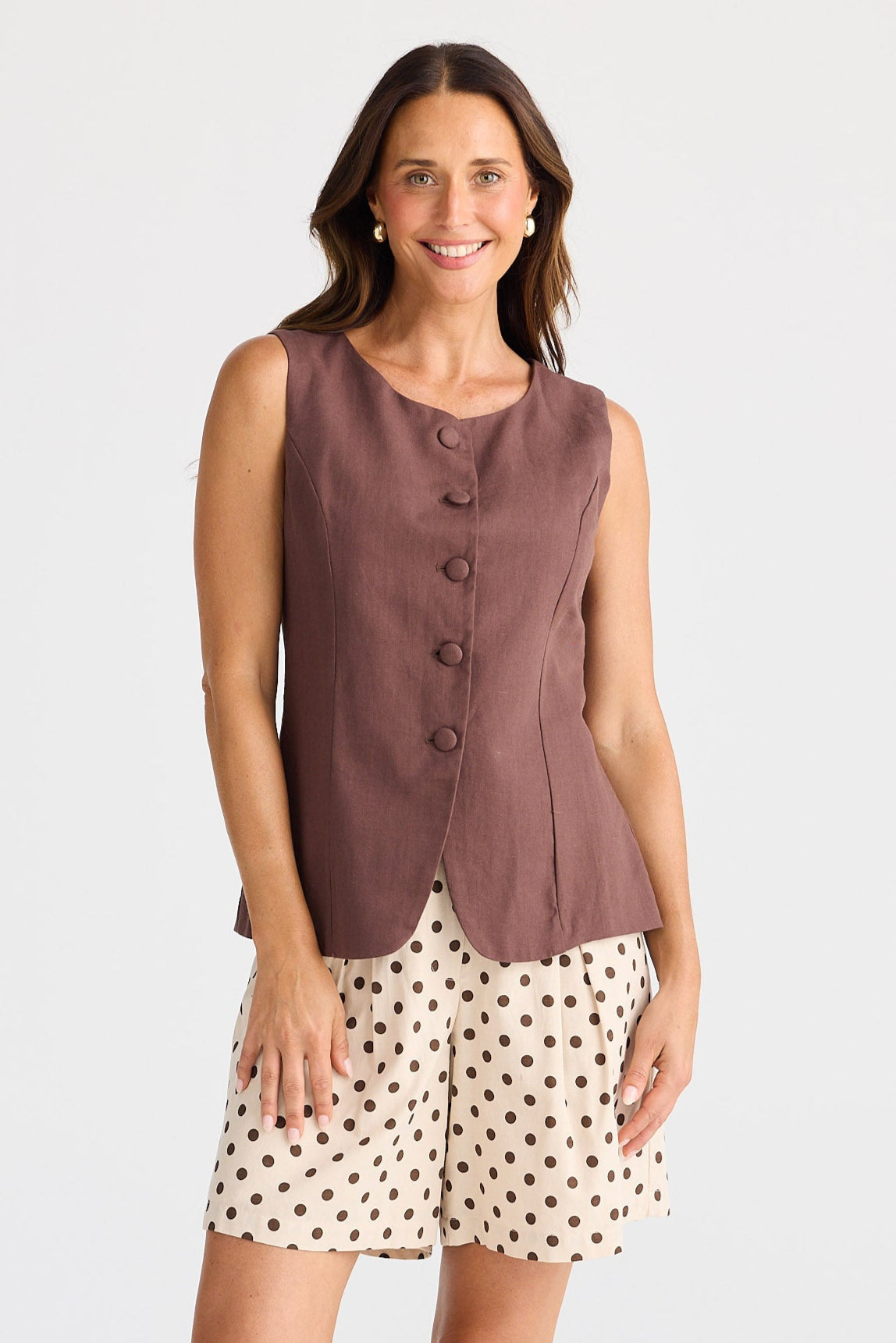 Woman wearing a sleeveless brown top and polka dot shorts on a white background