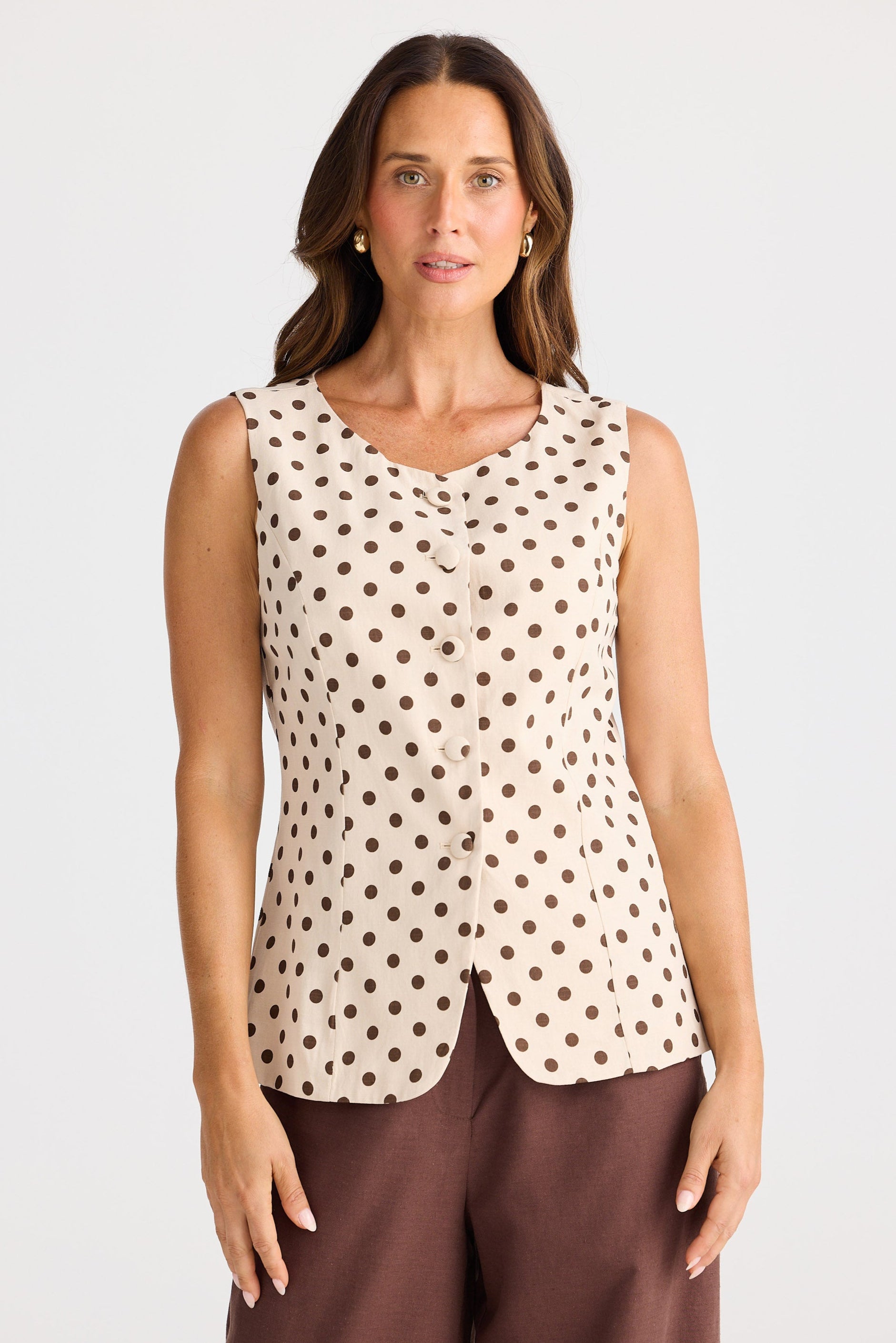 Woman wearing a sleeveless polka dot top and brown pants on a white background