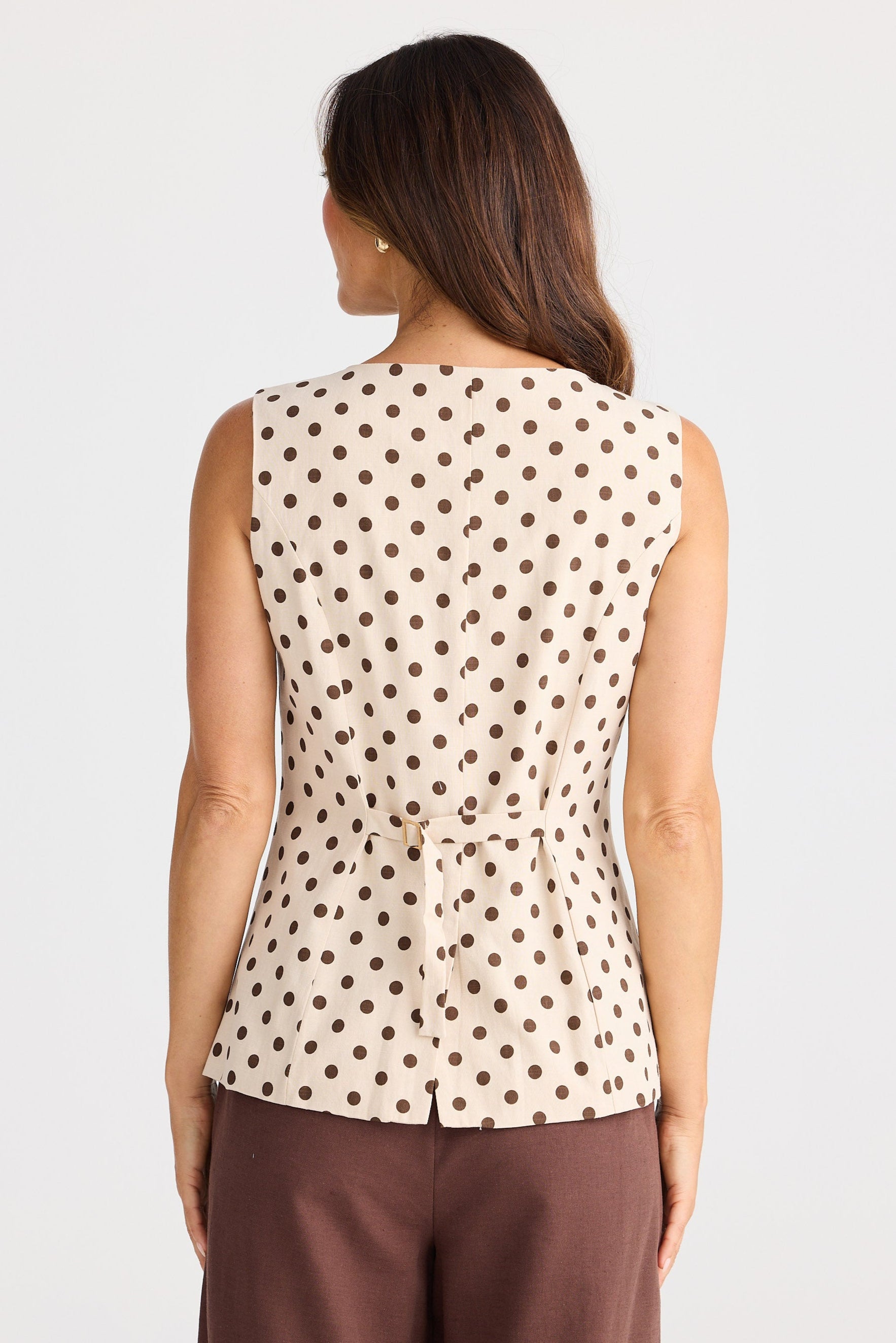 Woman wearing a sleeveless polka dot top and brown pants on a white background