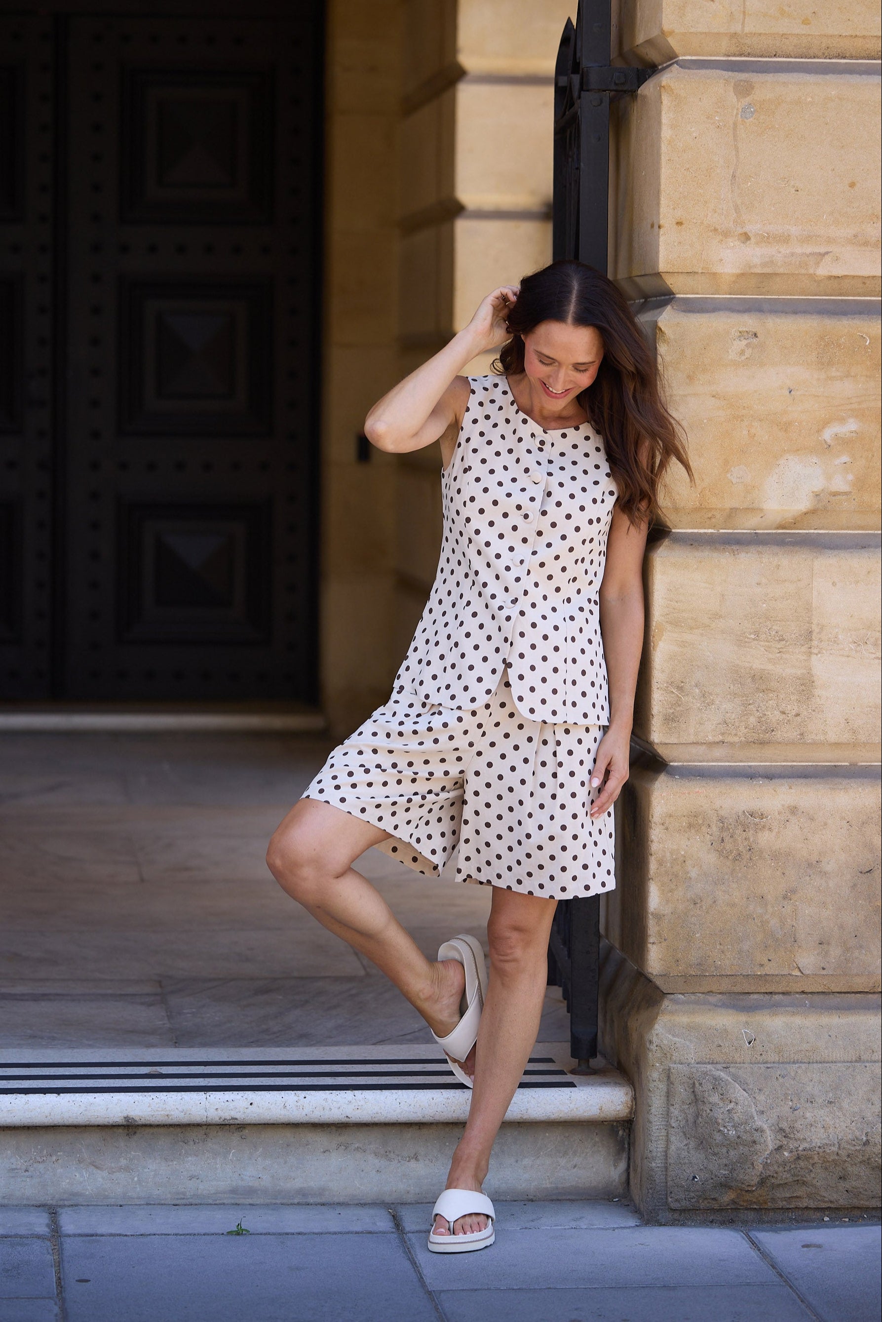 Woman in a polka dot dress standing against a stone wall.