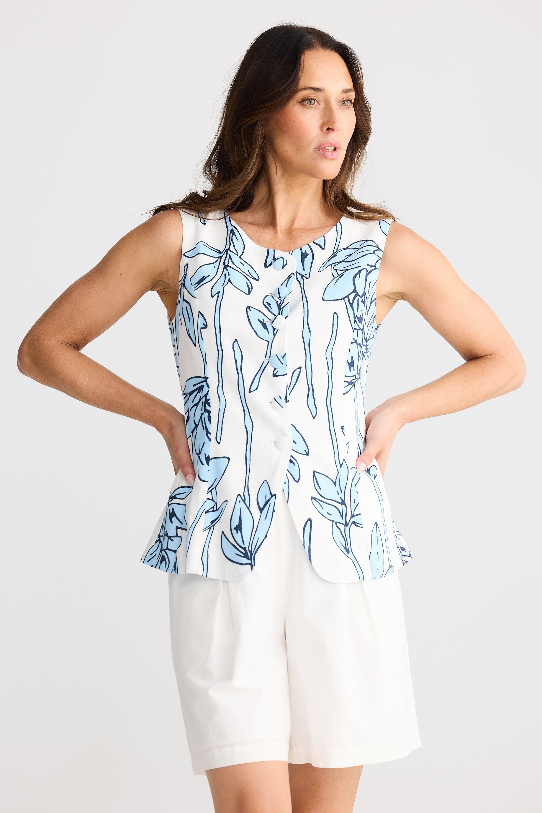 Woman wearing a sleeveless blue and white patterned top with a plain white background