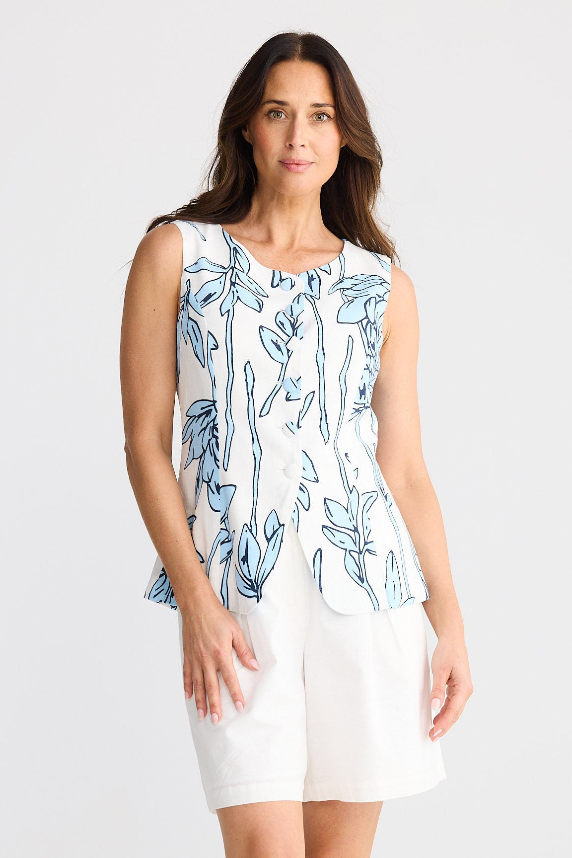 Woman wearing a sleeveless floral top and white shorts on a plain background