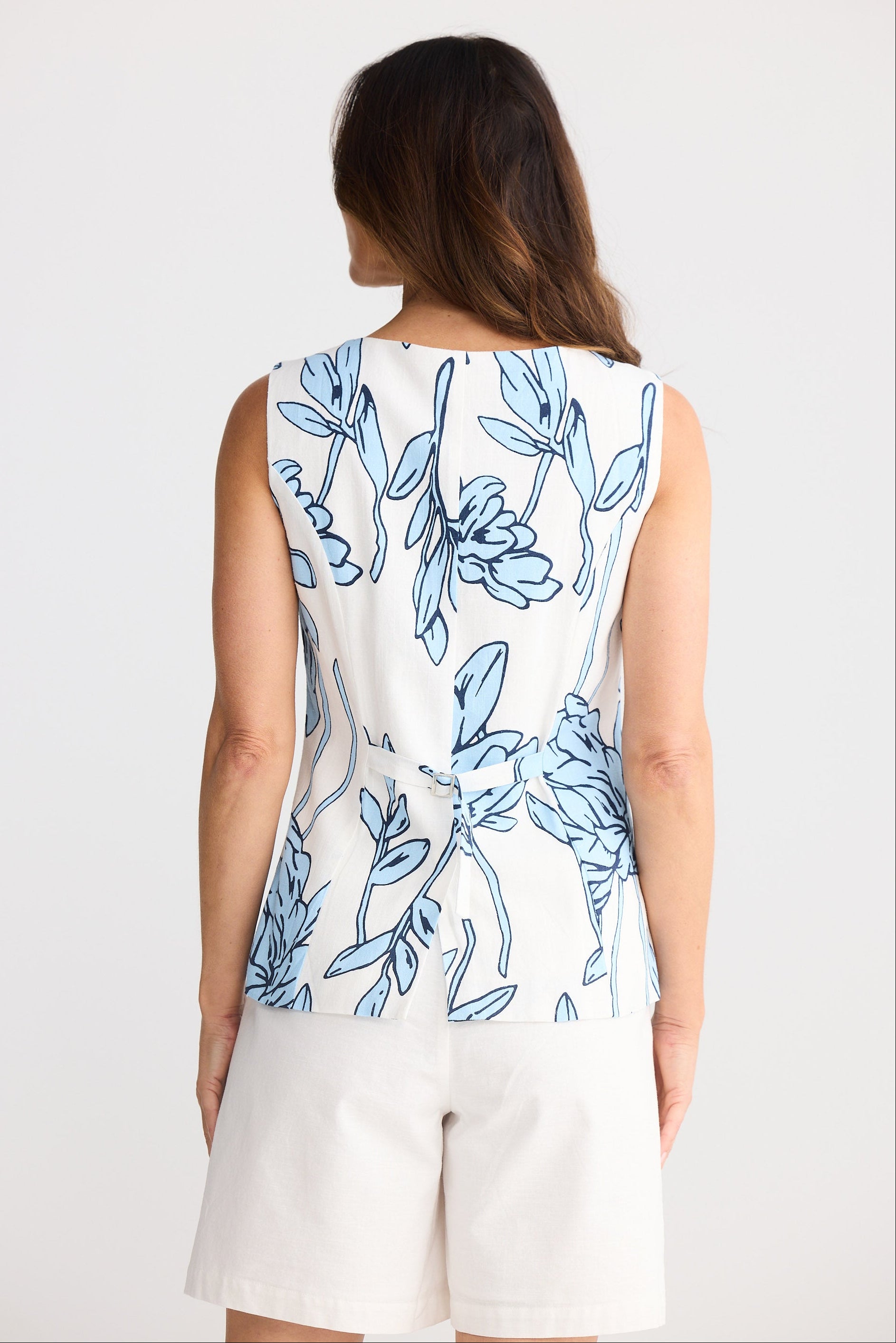 Woman wearing a sleeveless top with blue floral pattern on a plain background