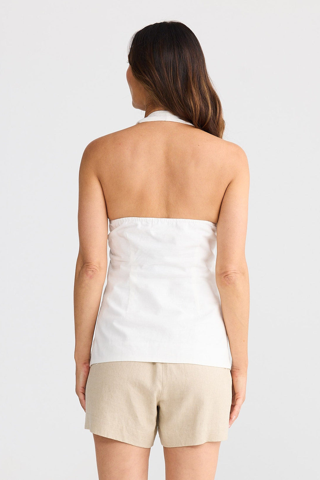 Woman wearing a white strapless top and beige shorts on a white background