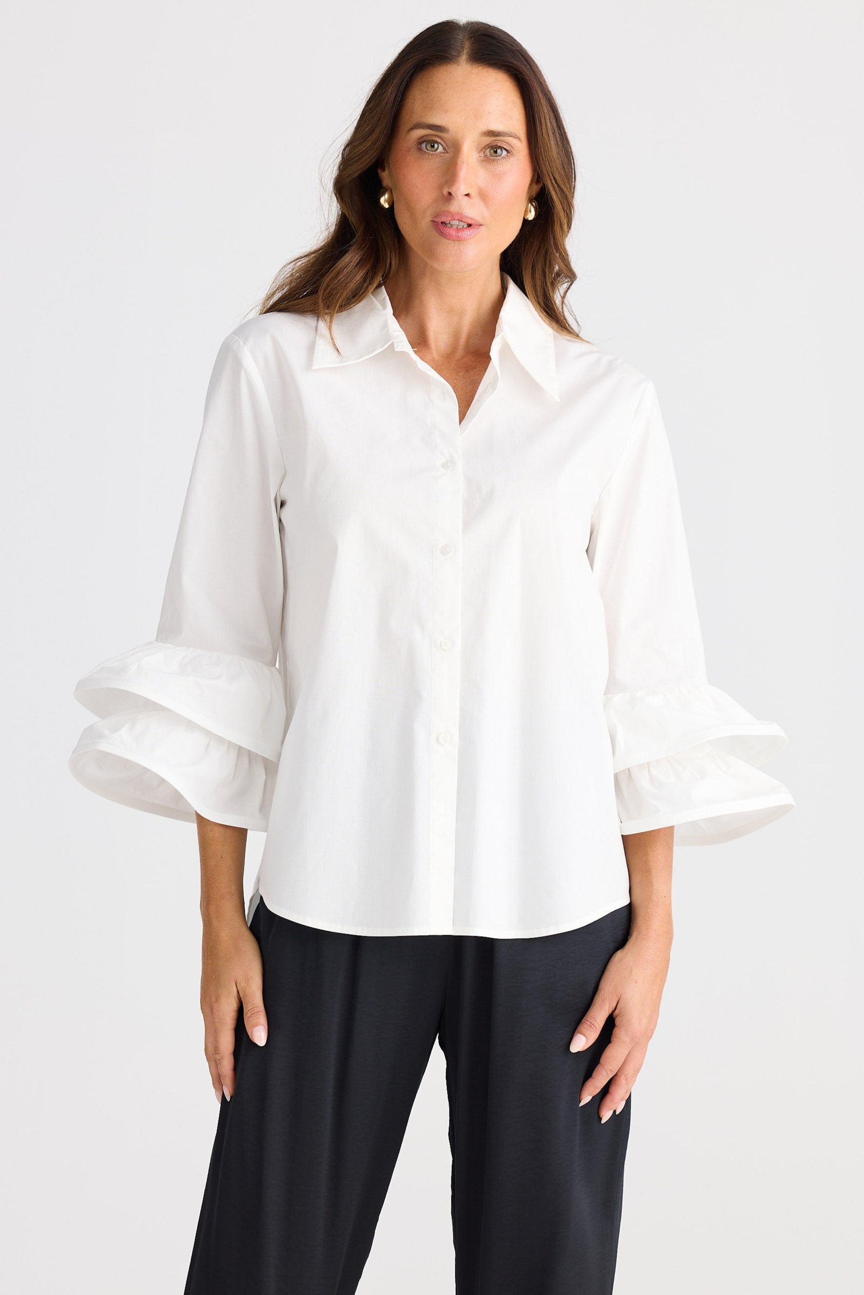 Woman wearing a white blouse with ruffled sleeves on a plain background