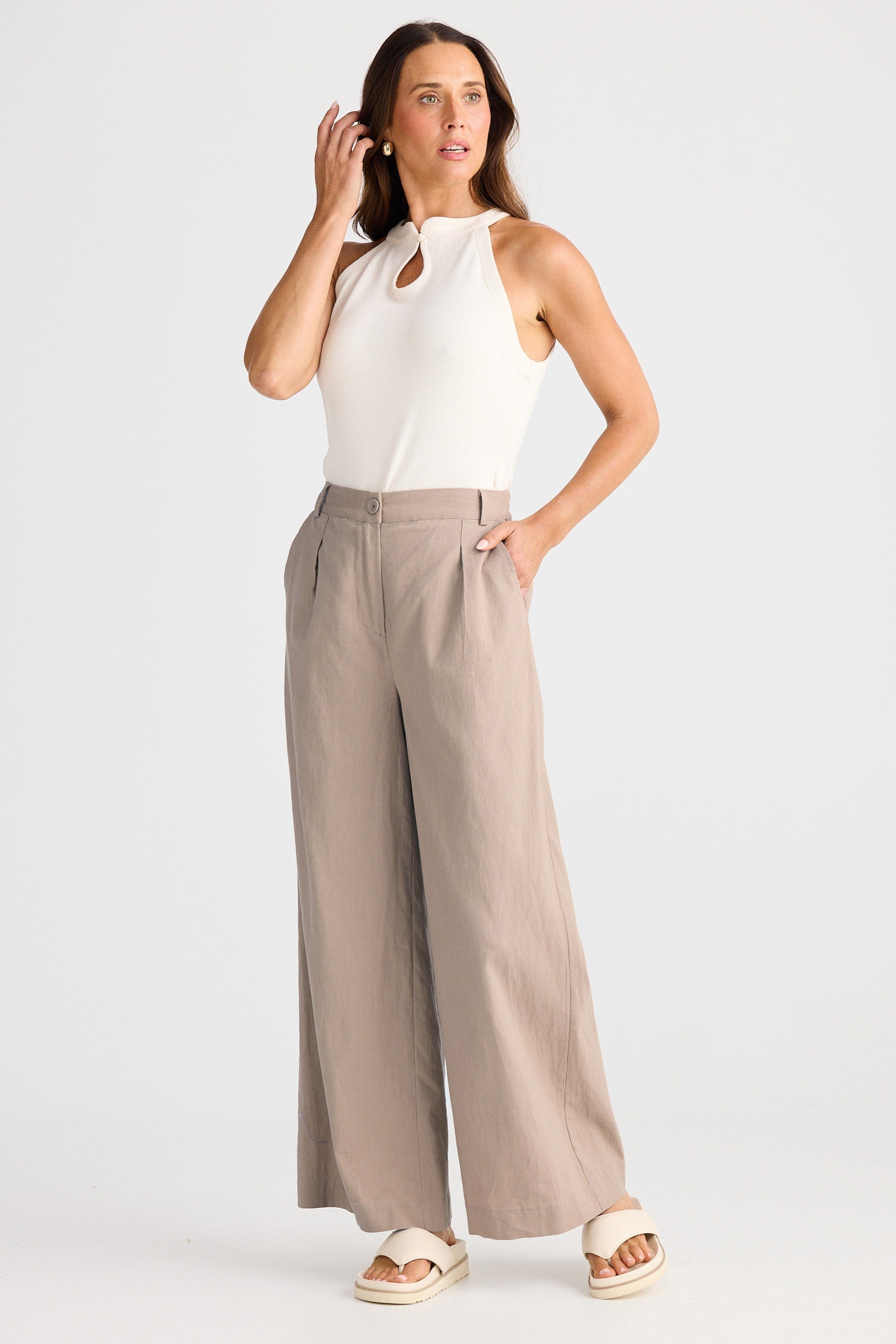 Woman wearing a white sleeveless top and beige wide-leg pants on a white background