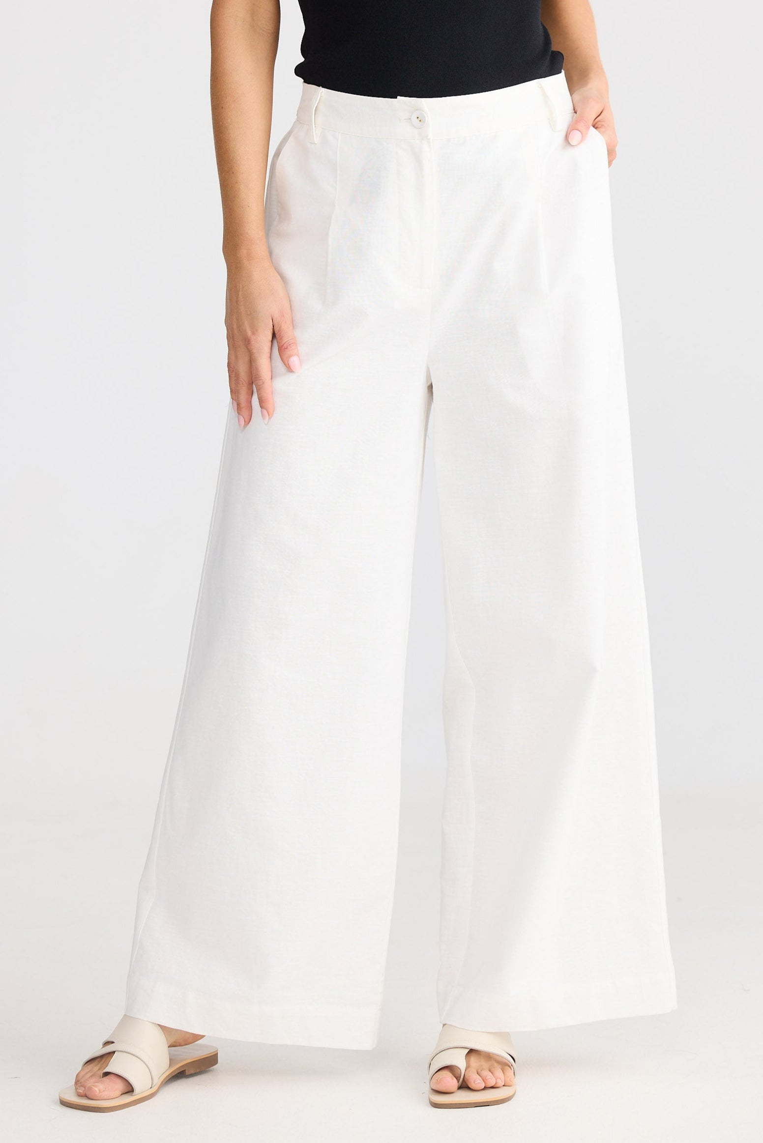 Person wearing a black tank top and white wide-leg pants on a white background