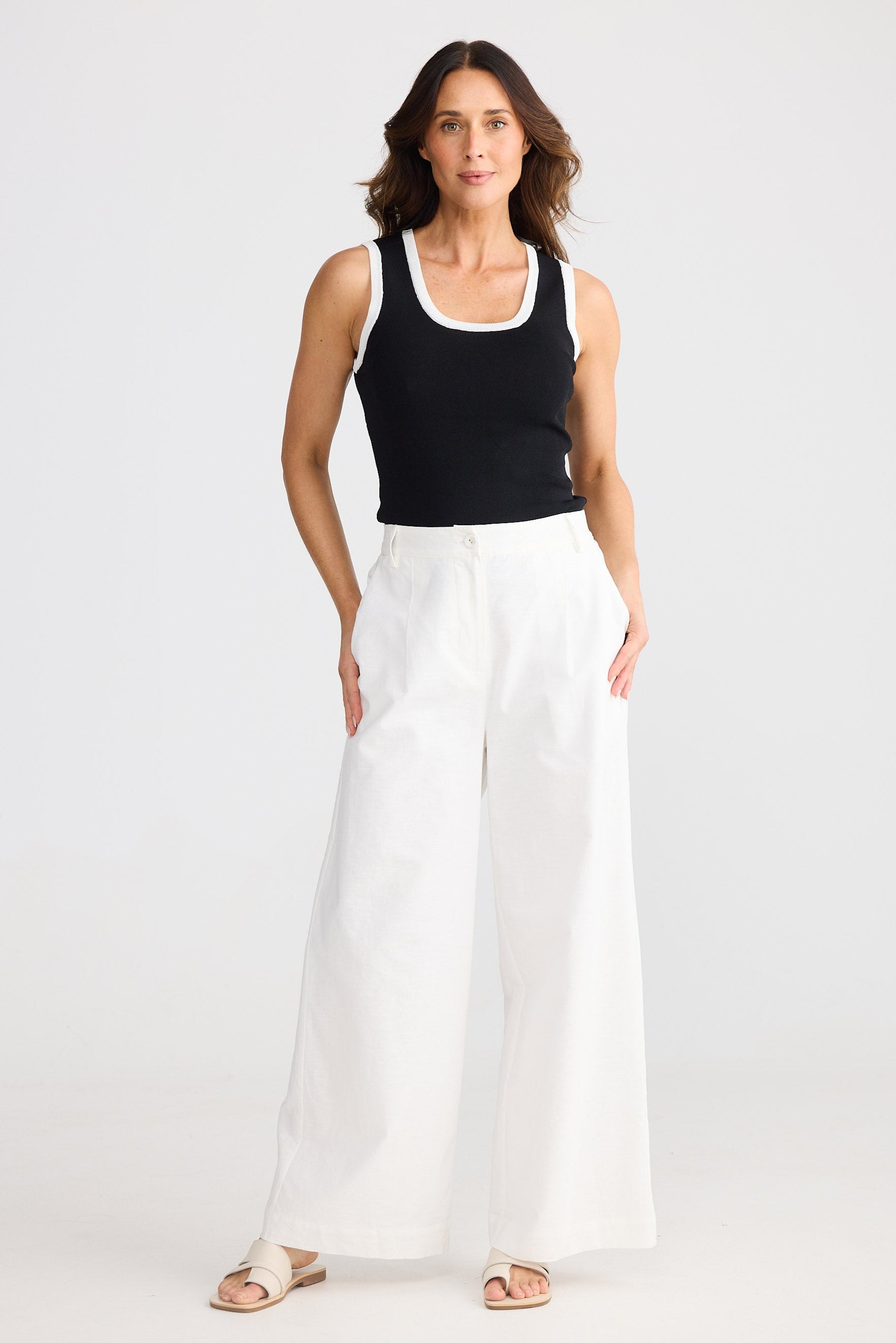 Woman wearing a black tank top and white pants on a white background
