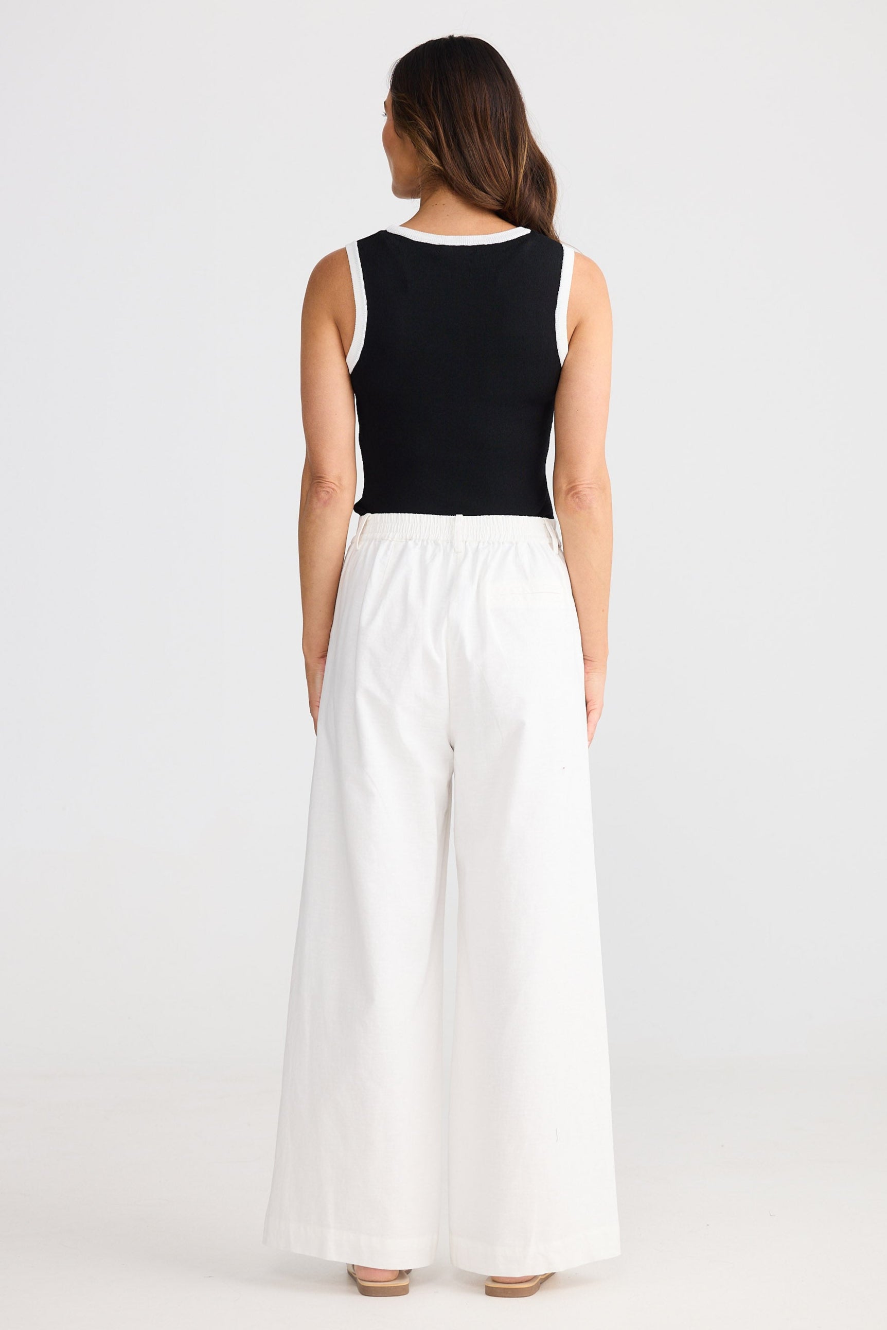 Woman wearing a black sleeveless top and white wide-leg pants on a white background