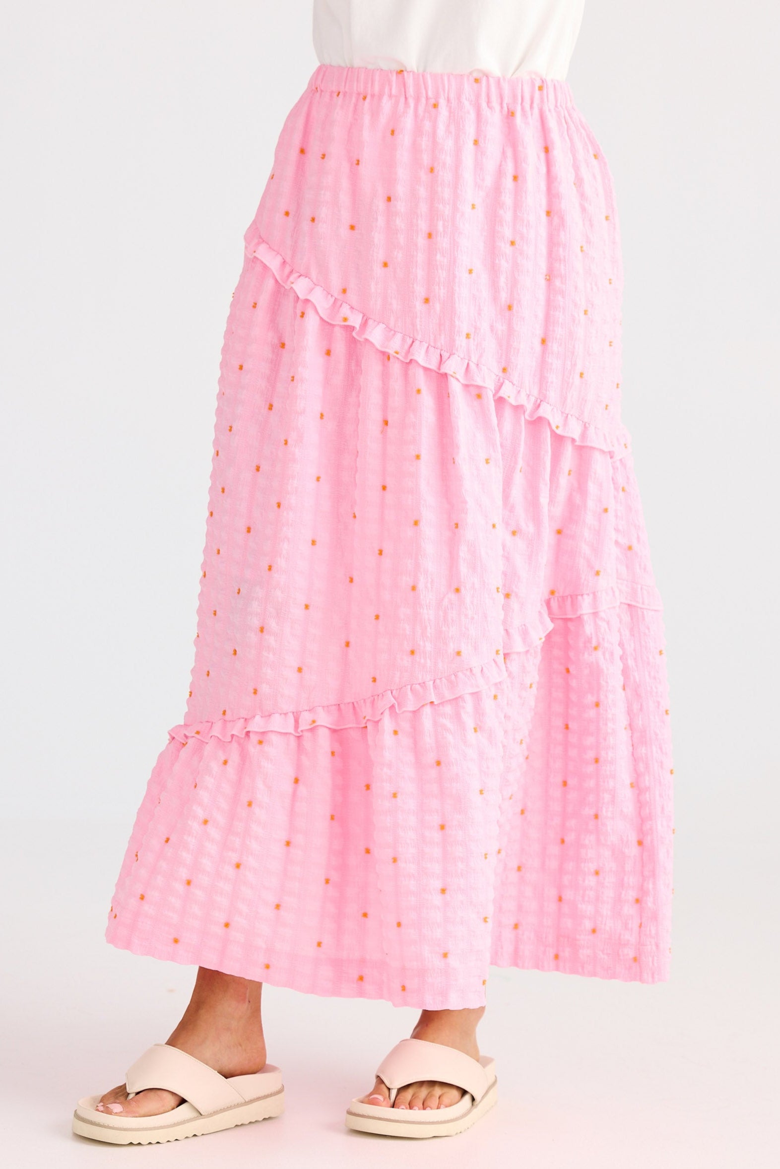 Person wearing a white top and pink skirt with gold polka dots on a light gray background