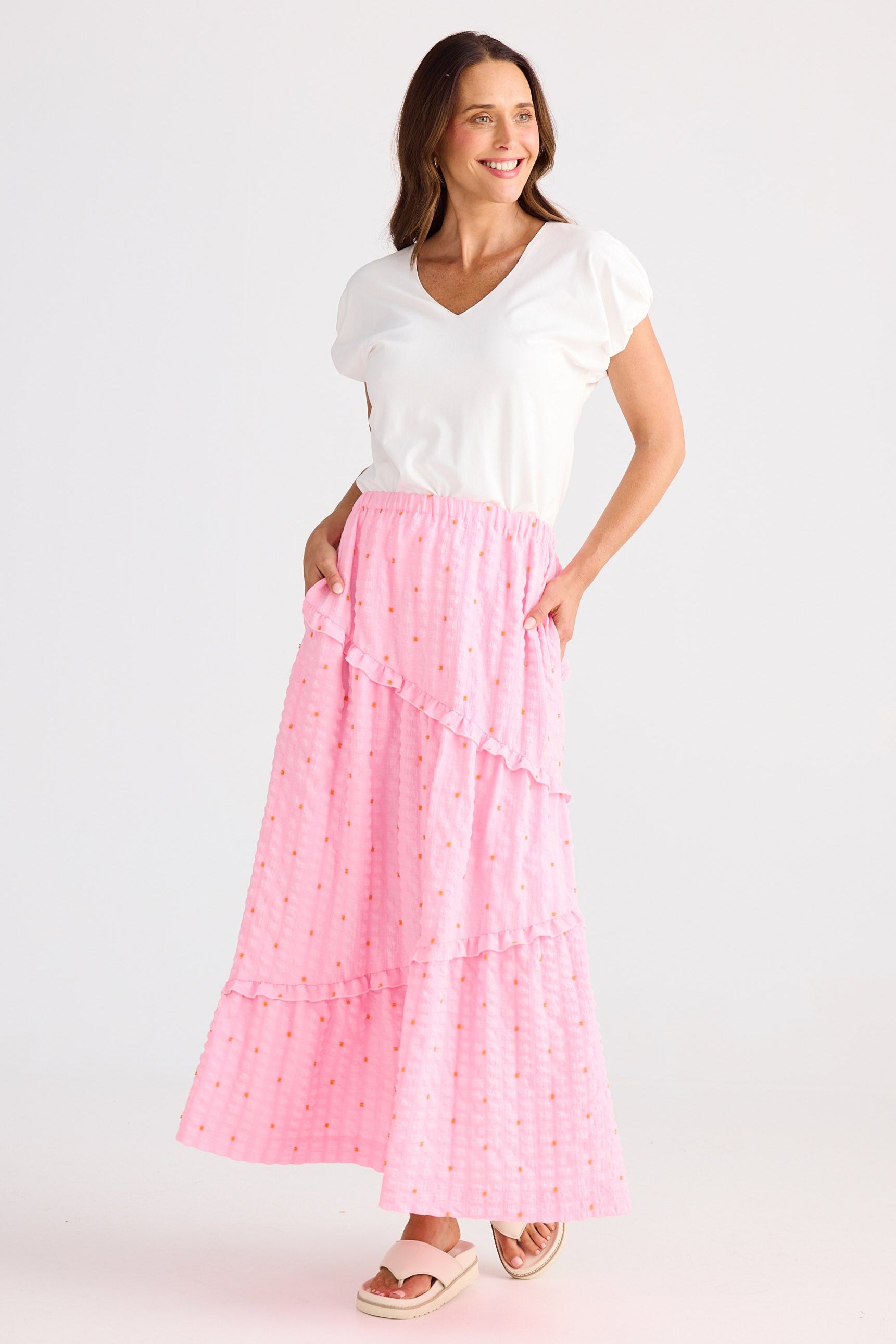 Woman wearing a white top and pink skirt on a light gray background