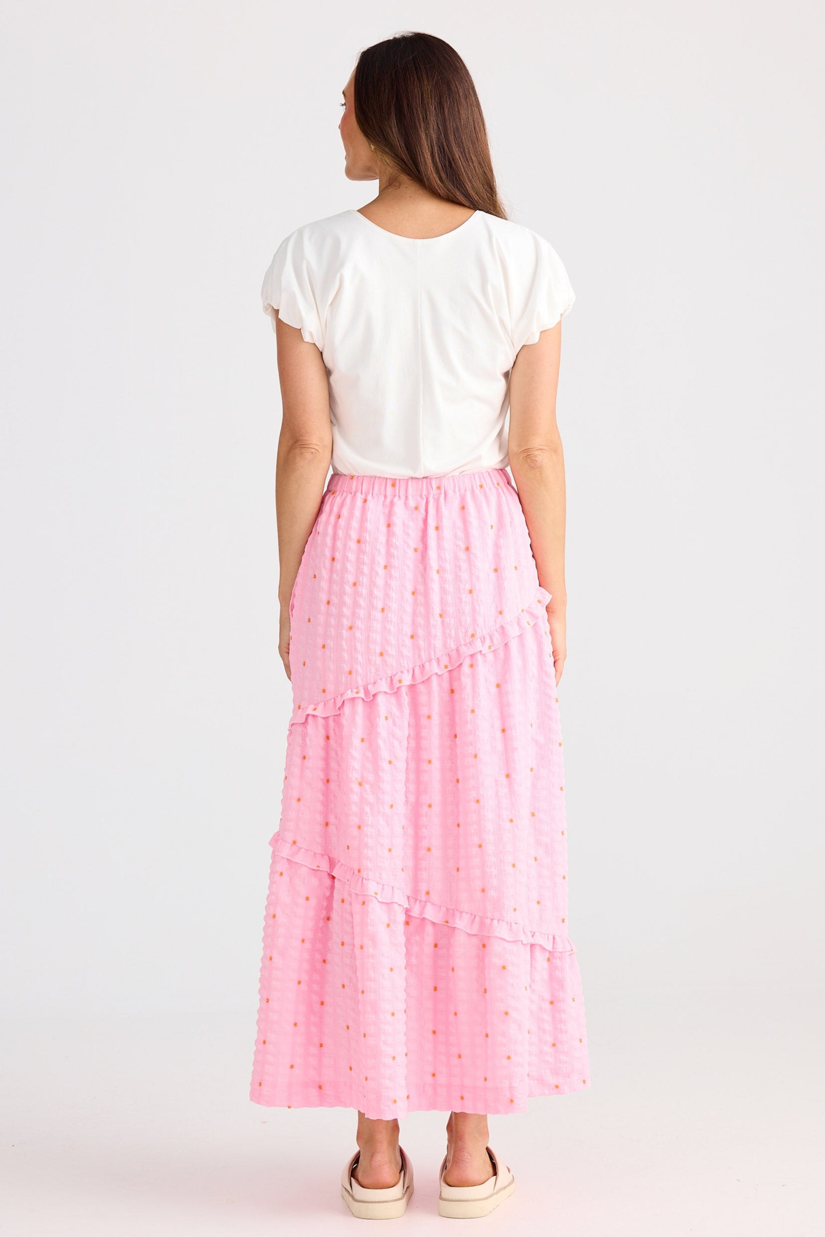 Woman wearing a white top and pink tiered skirt on a white background