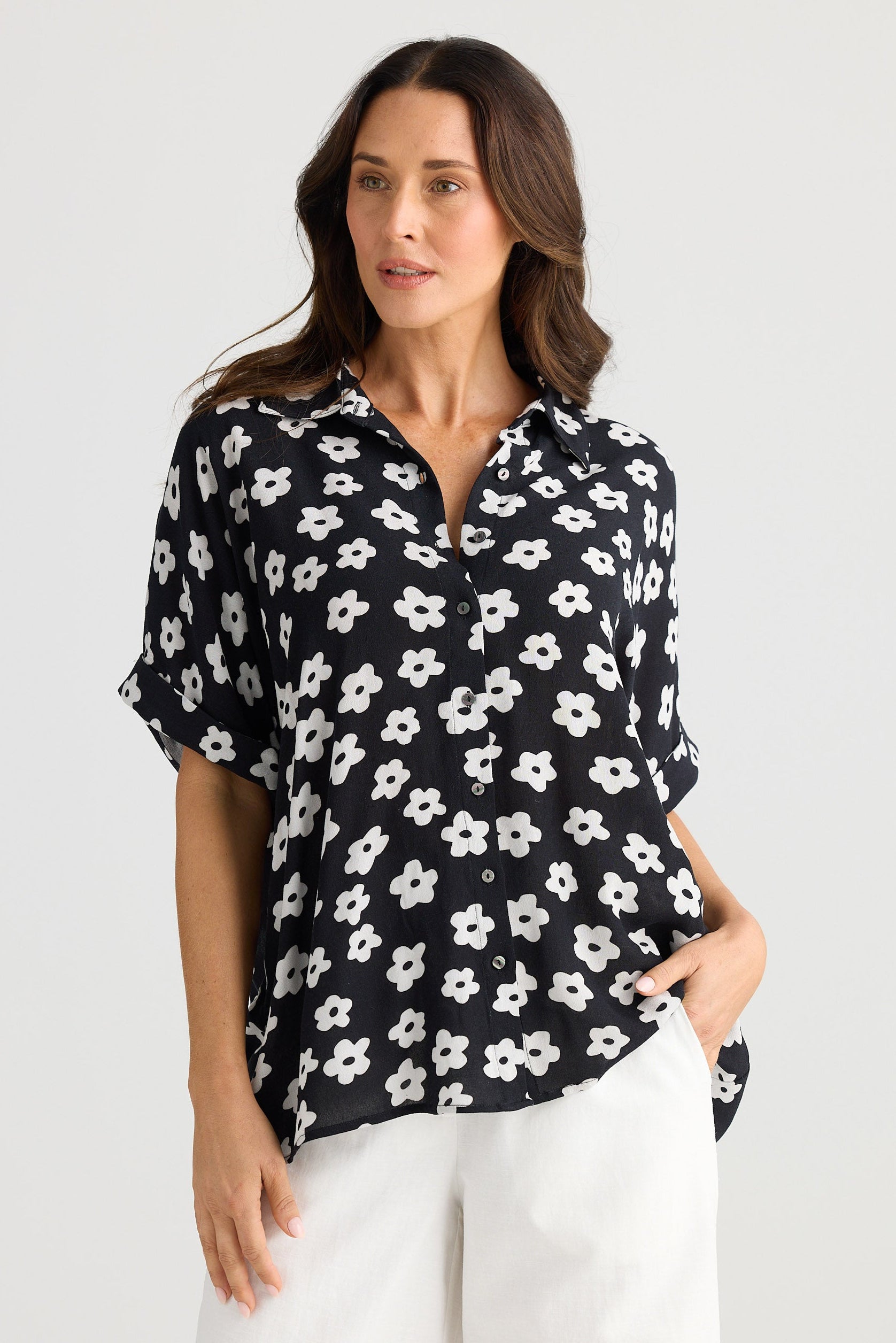 Woman wearing a black floral blouse with white pants on a light gray background