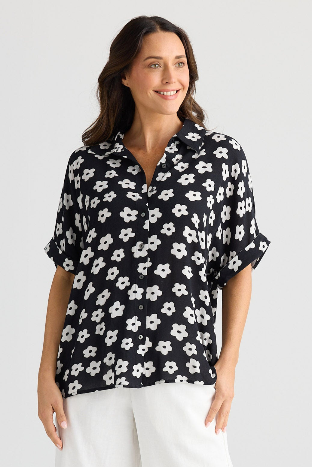Woman wearing a black floral blouse and white pants on a white background