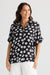Woman wearing a black floral blouse and white pants on a white background