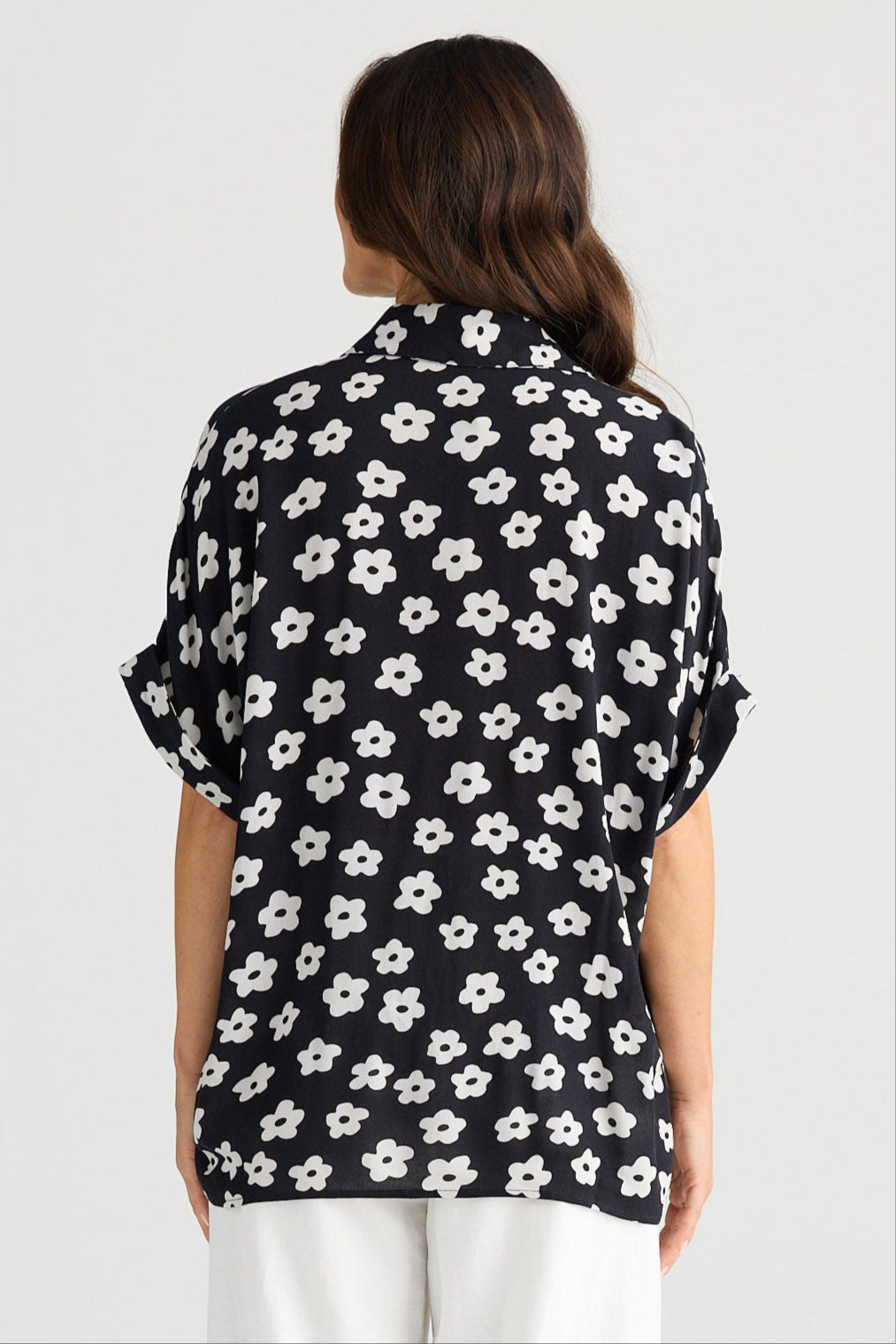 Person wearing a black floral blouse and white pants on a white background