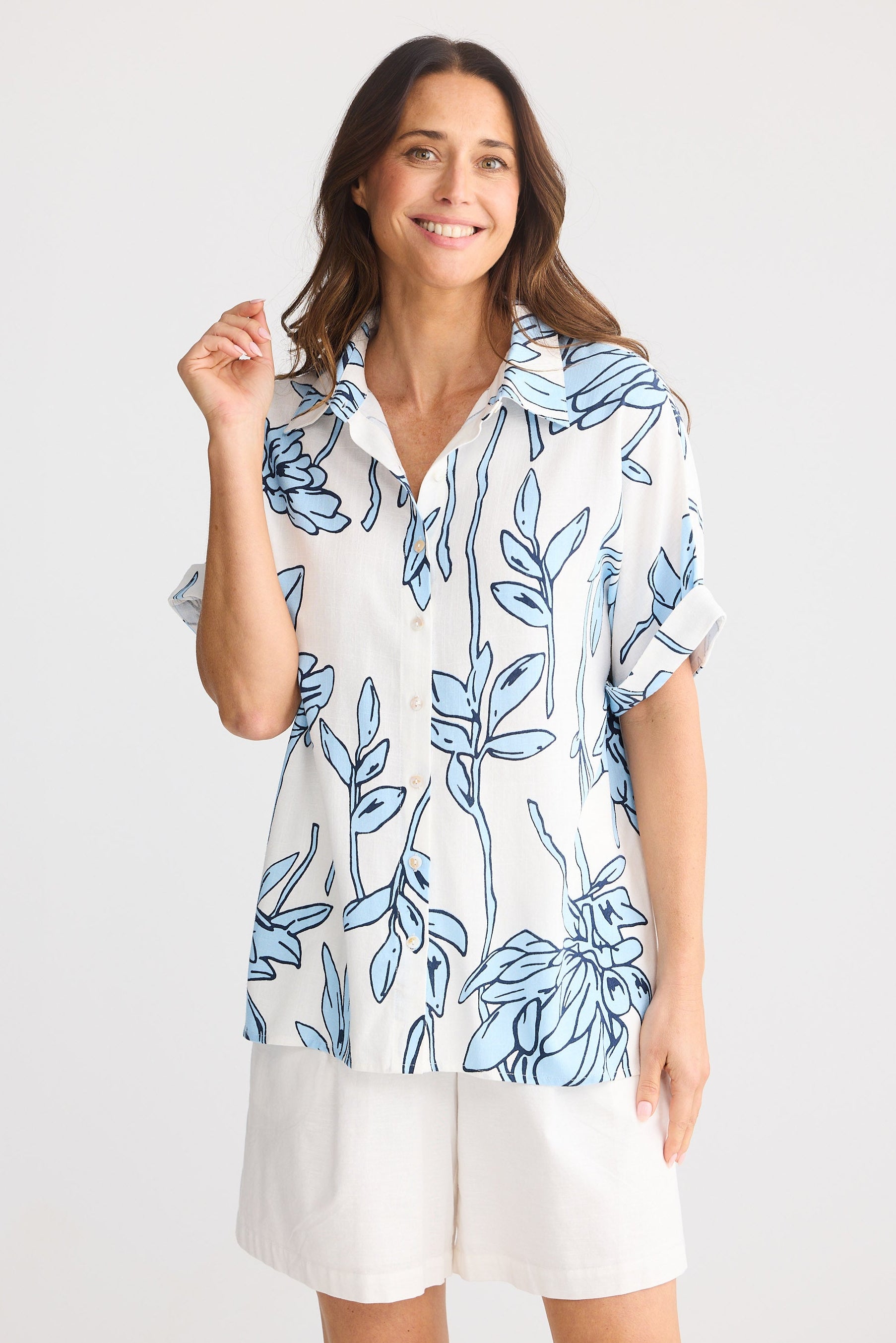 Woman wearing a white blouse with blue floral pattern and white shorts on a white background