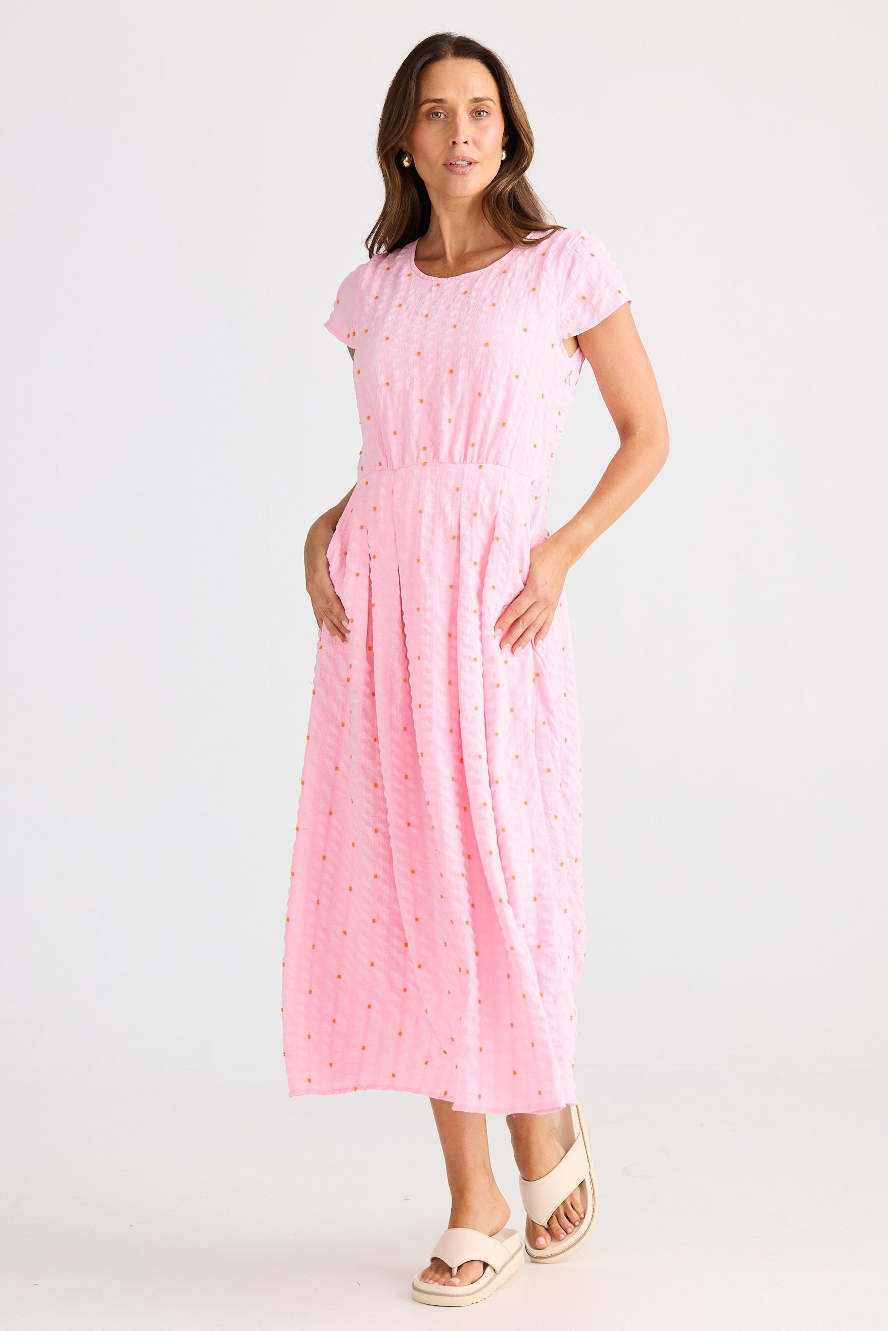 Woman wearing a pink dress with white polka dots on a white background