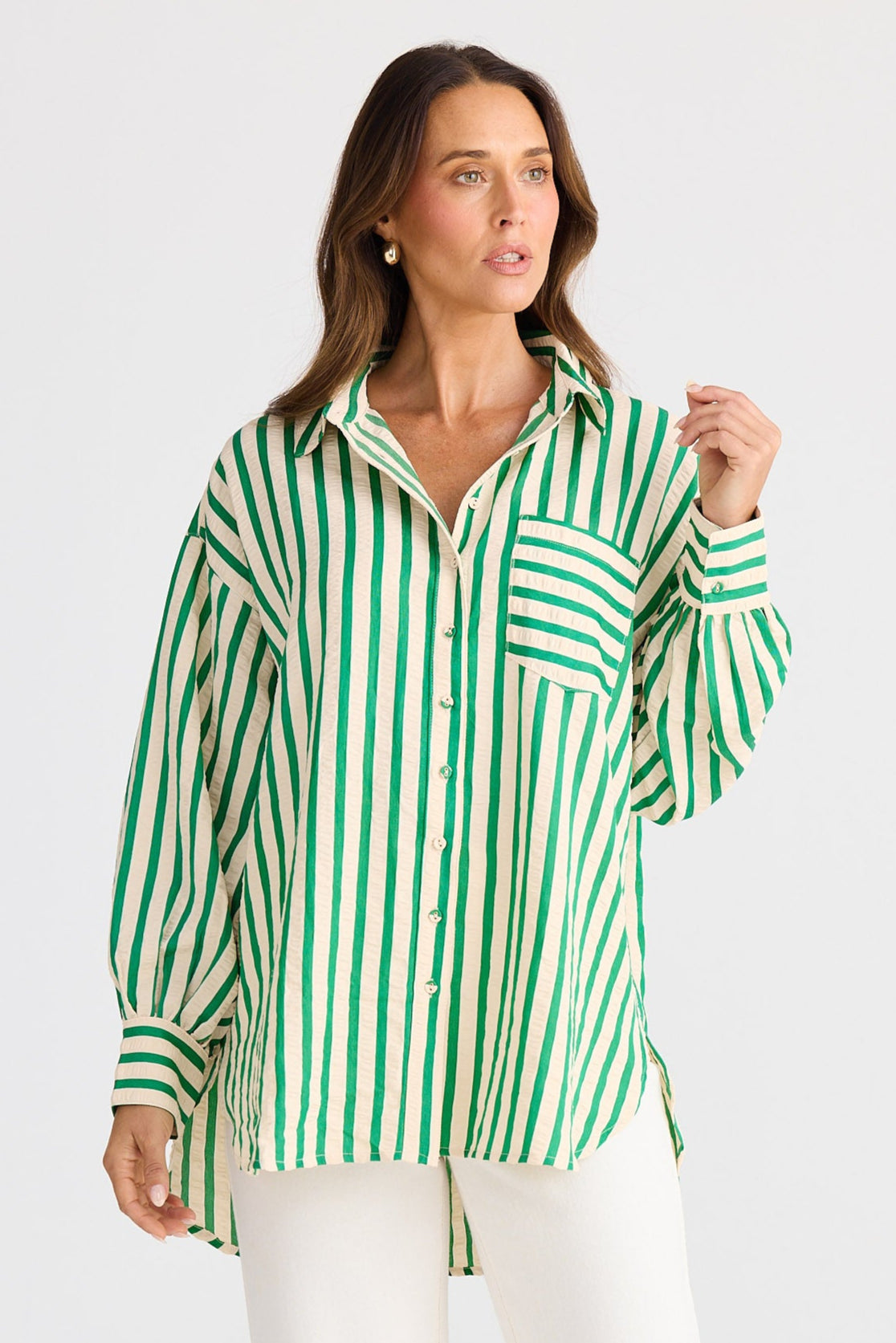 Woman wearing a green and white striped shirt with white pants on a light gray background