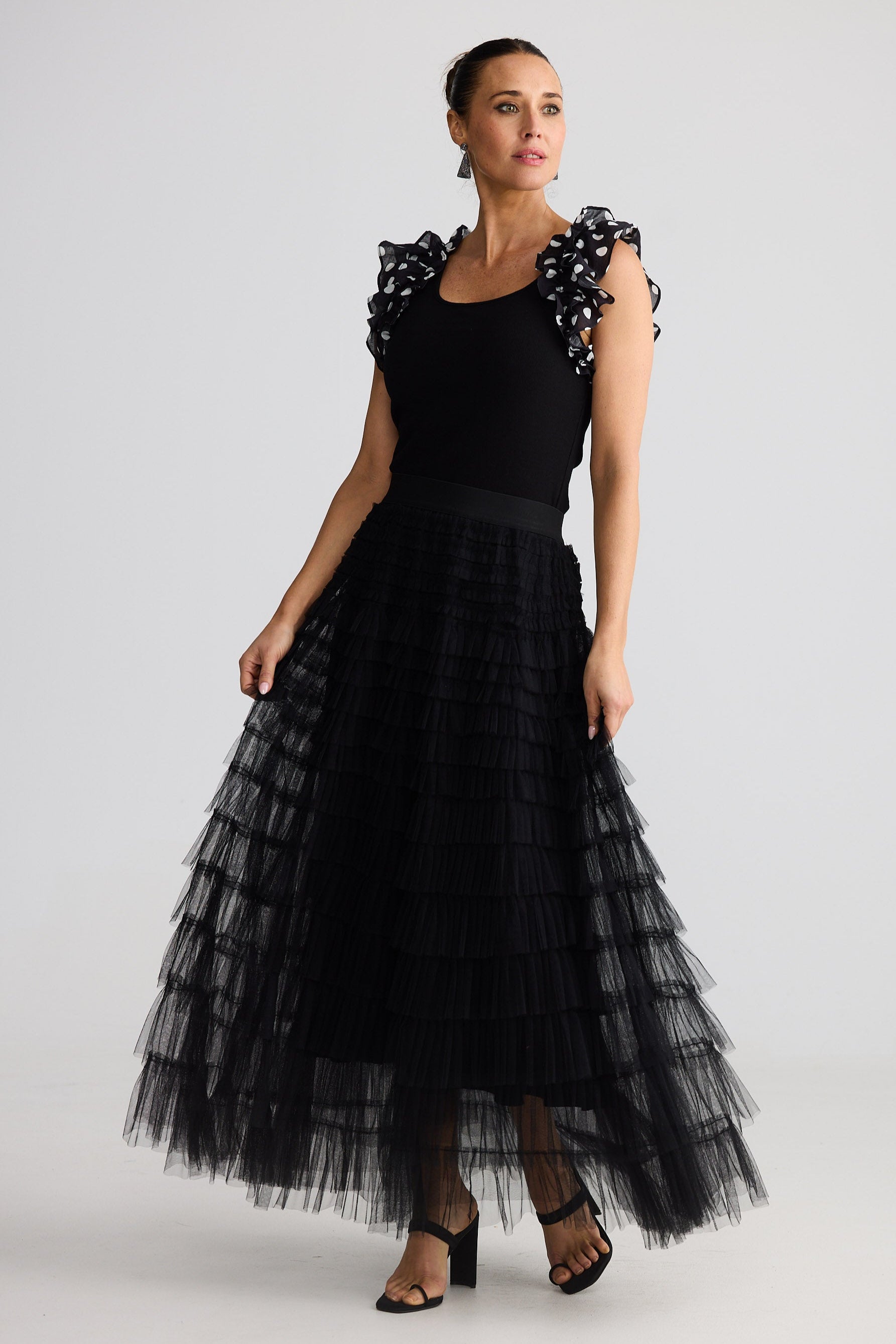 Woman wearing a black tiered skirt and black singlet ruffled sleeves on a white background