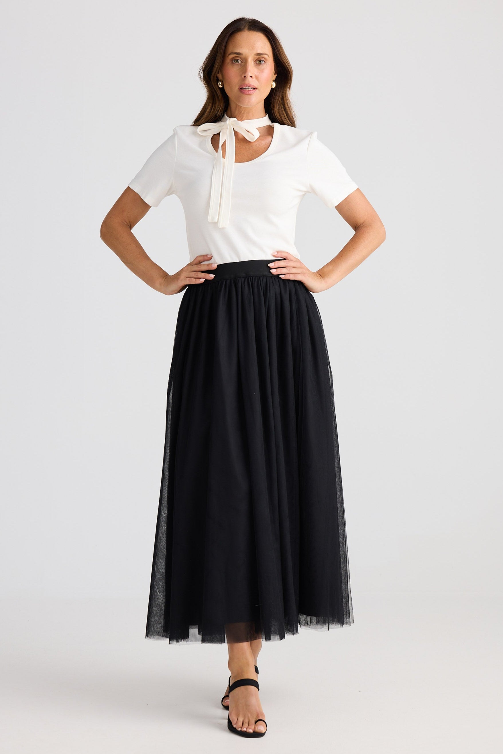 Woman wearing a white top with a bow and a black tulle skirt on a white background