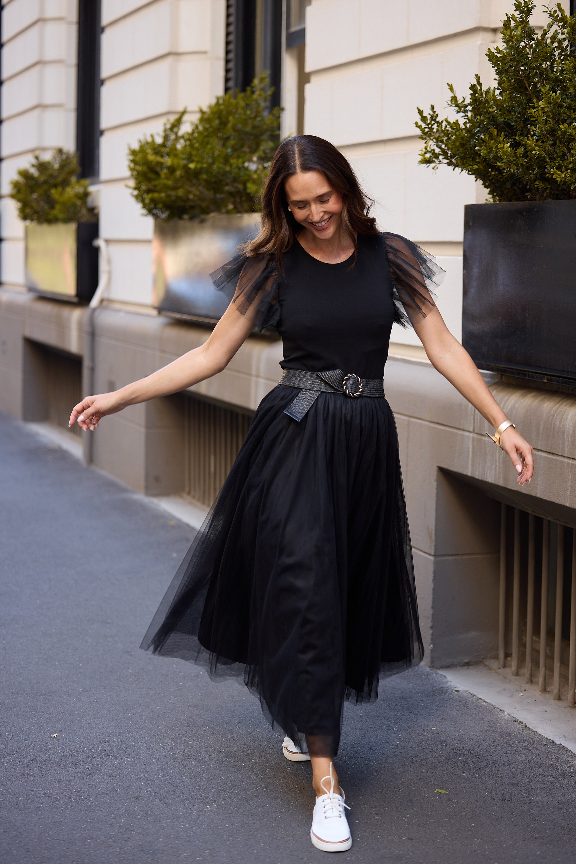 Woman in a black dress with white sneakers standing on a street.