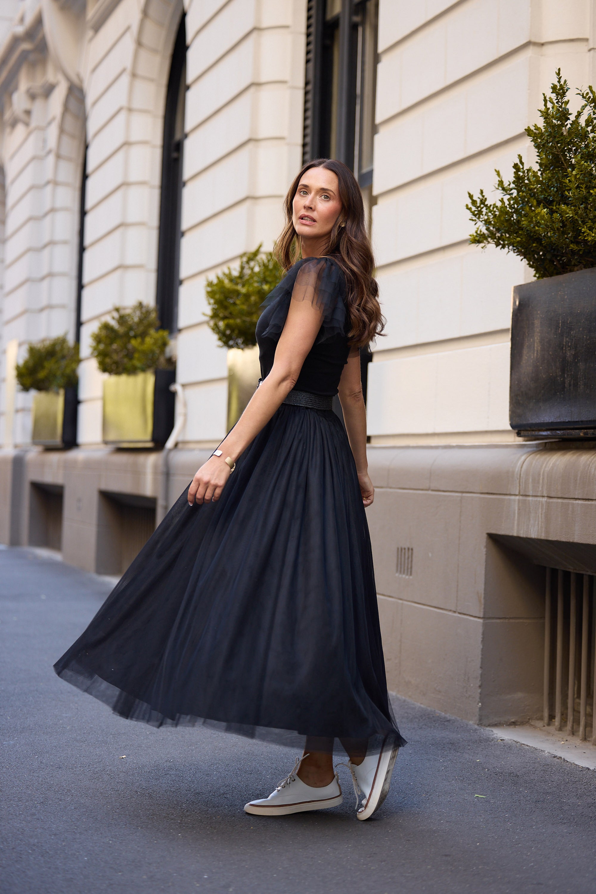 Woman in a black dress standing on a street with a building in the background