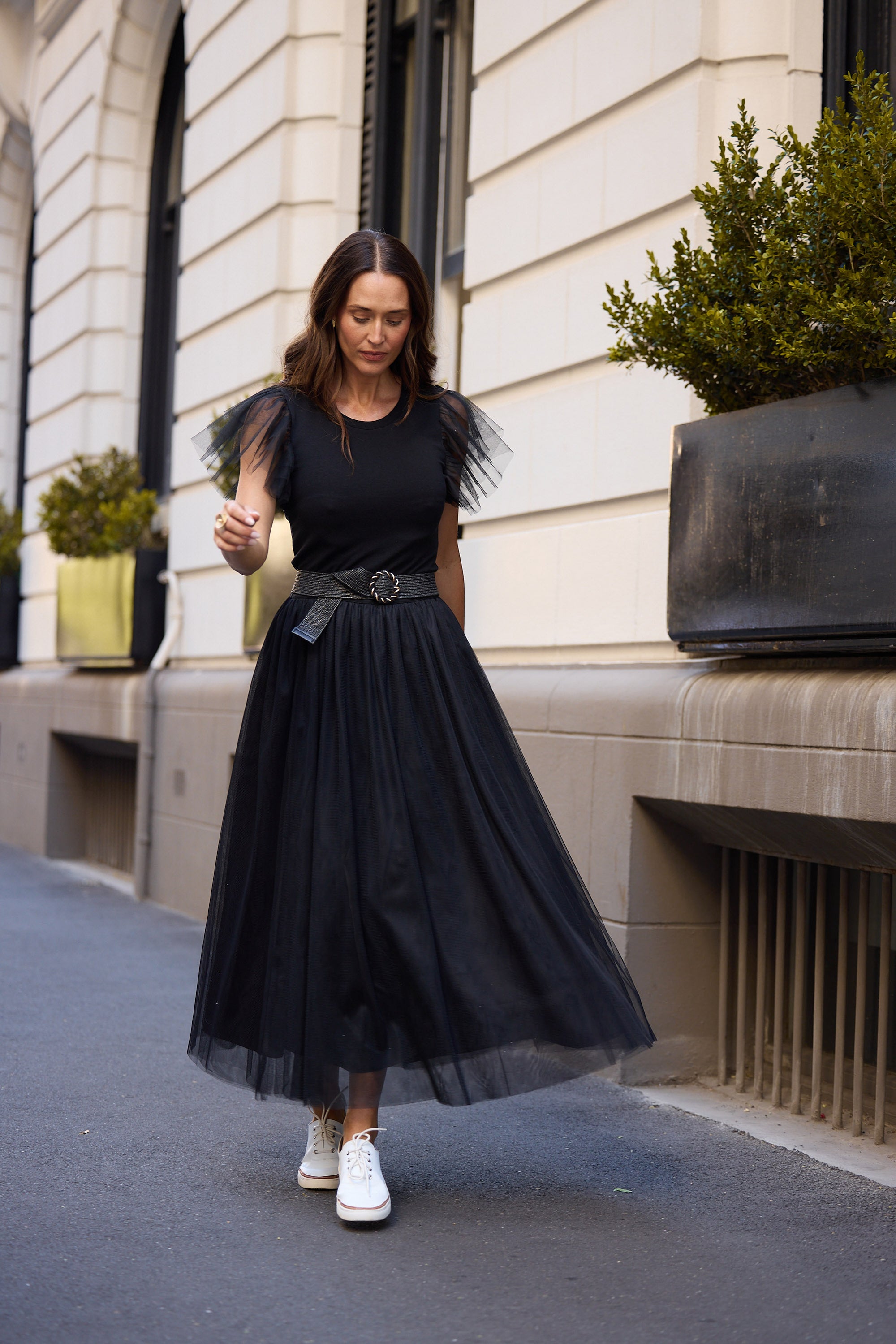 Woman in a black dress walking on a city street.