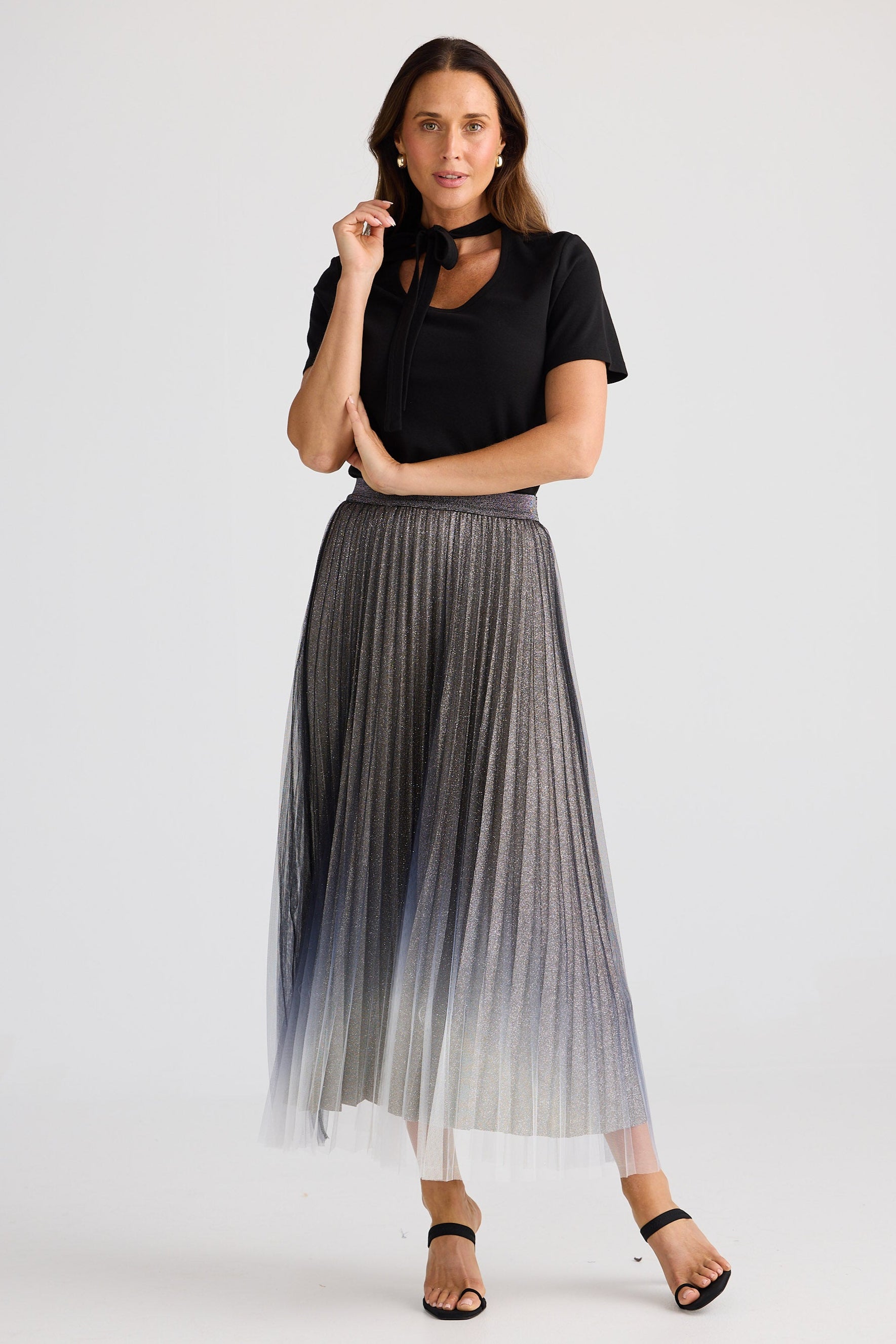 Woman wearing a black top and pleated silver skirt on a white background