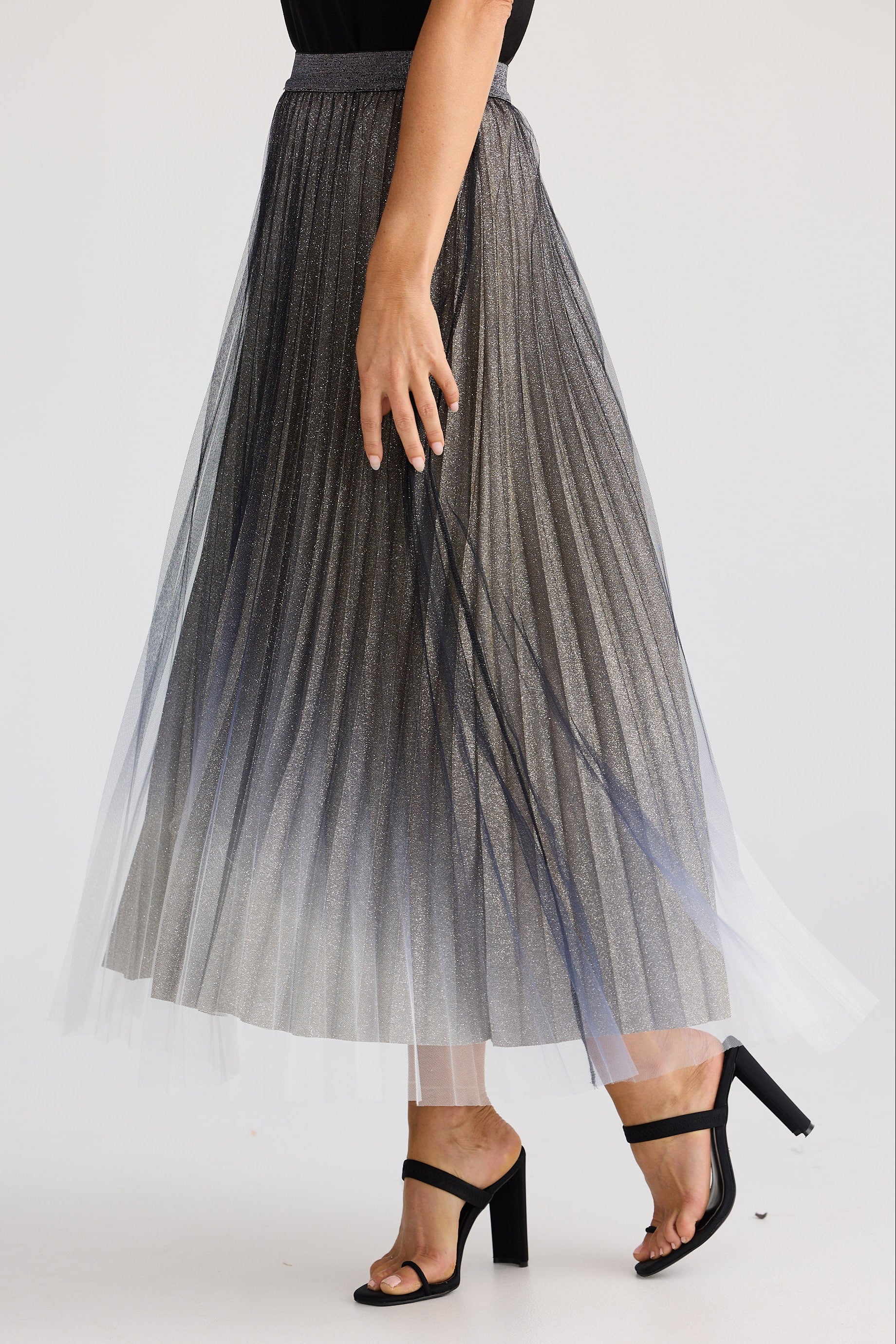 Person wearing a gray pleated skirt with black high-heeled shoes on a white background