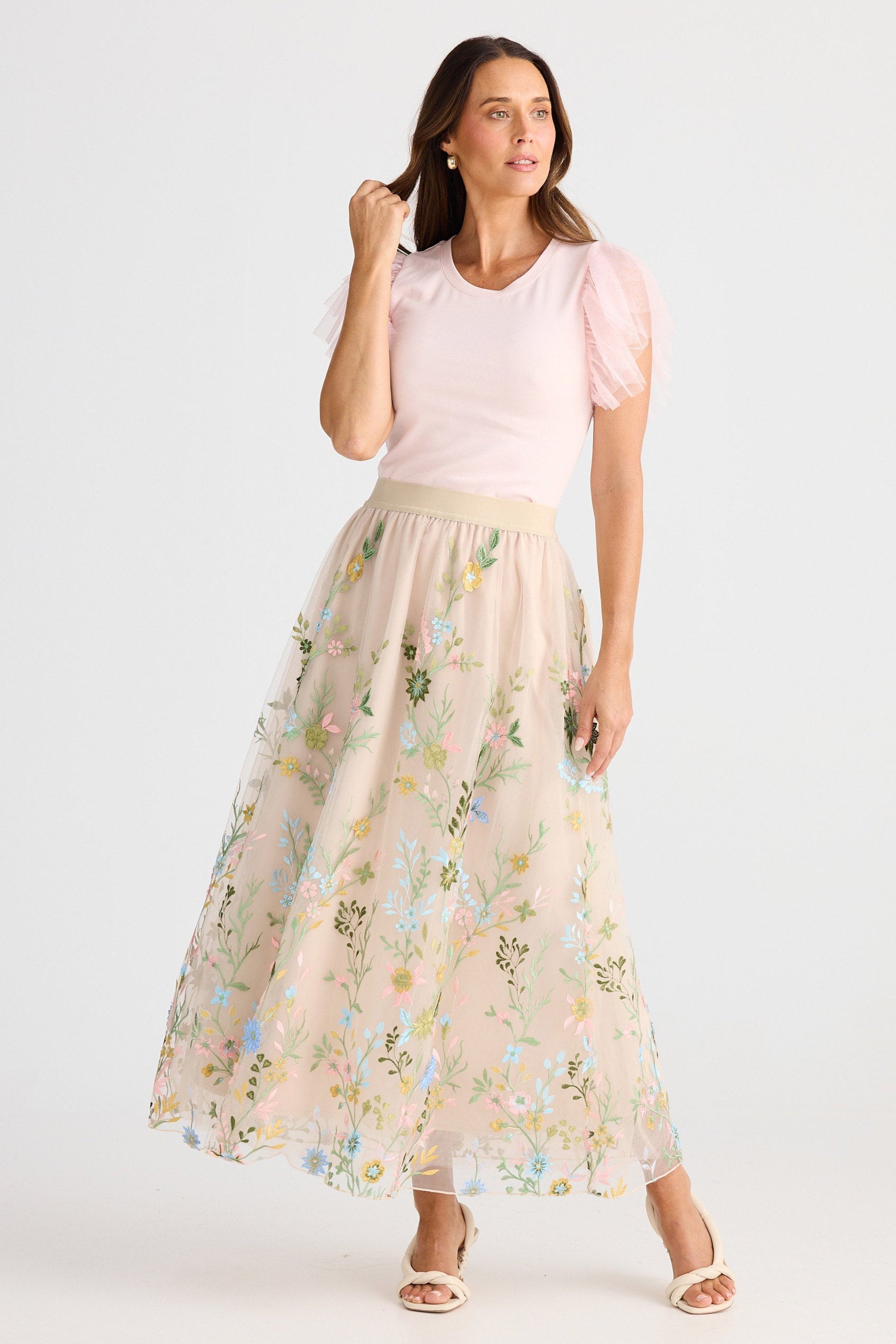 Woman wearing a light pink top and floral skirt on a white background