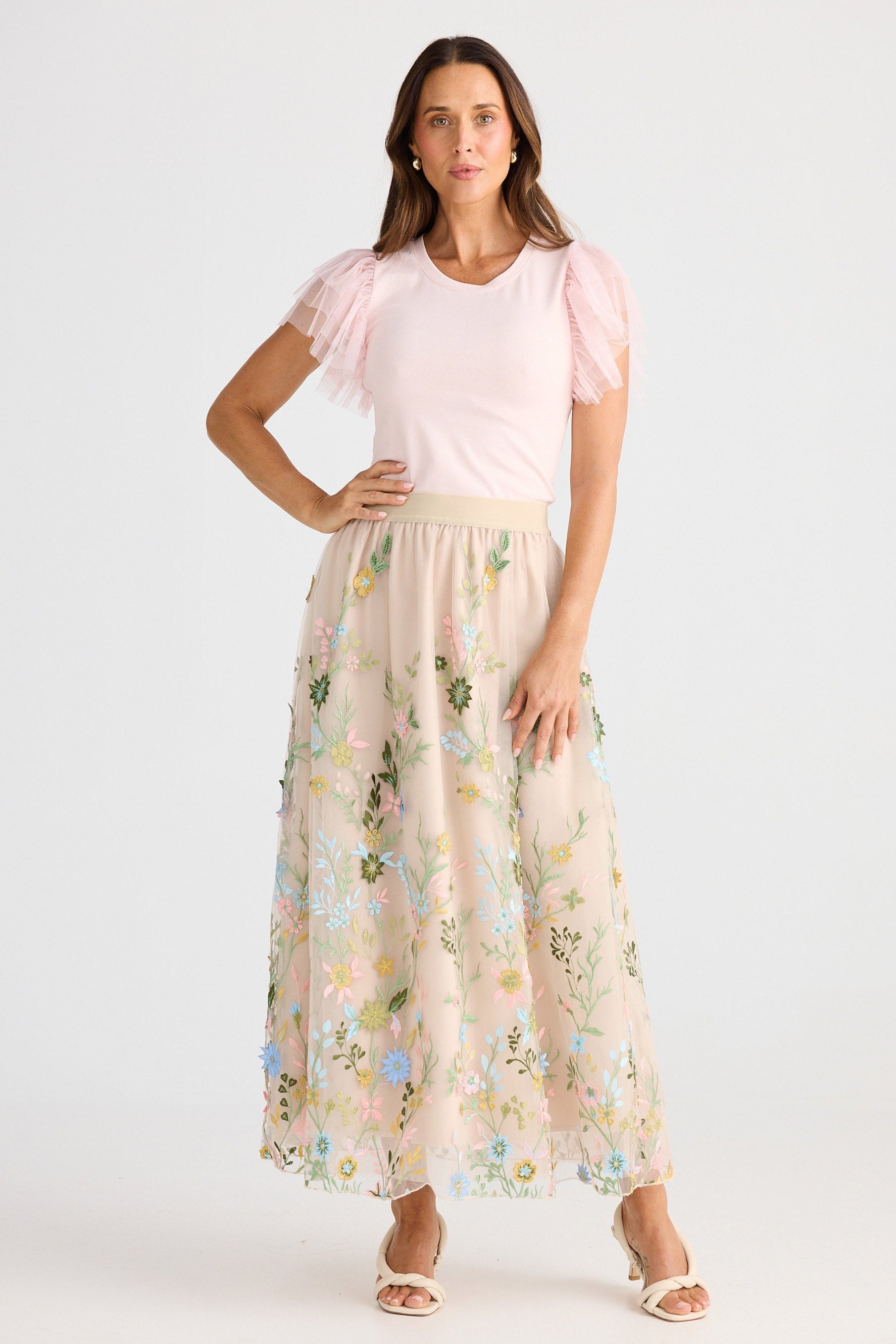 Woman wearing a pink top and floral skirt on a white background