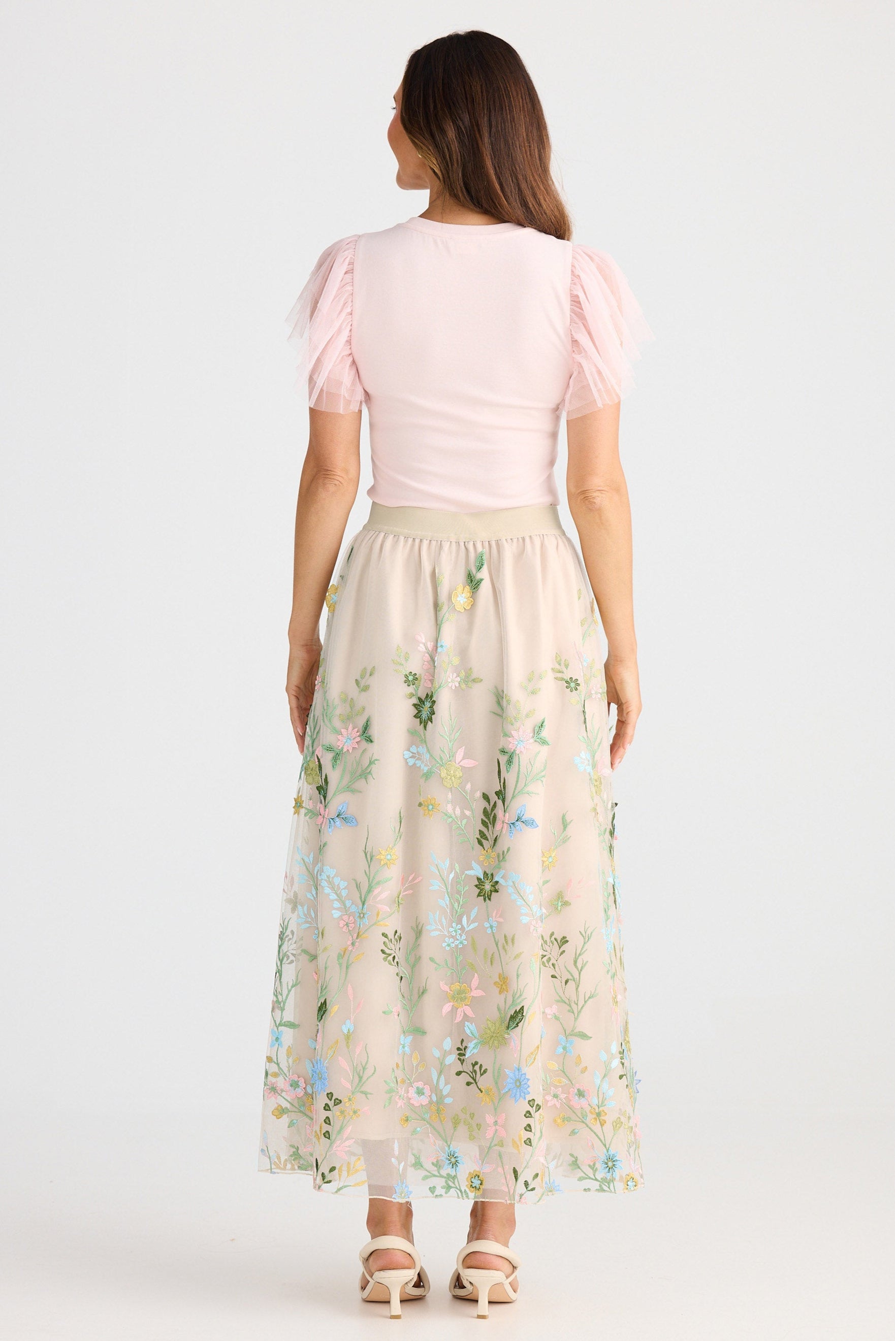 Woman wearing a light pink top and floral skirt on a white background