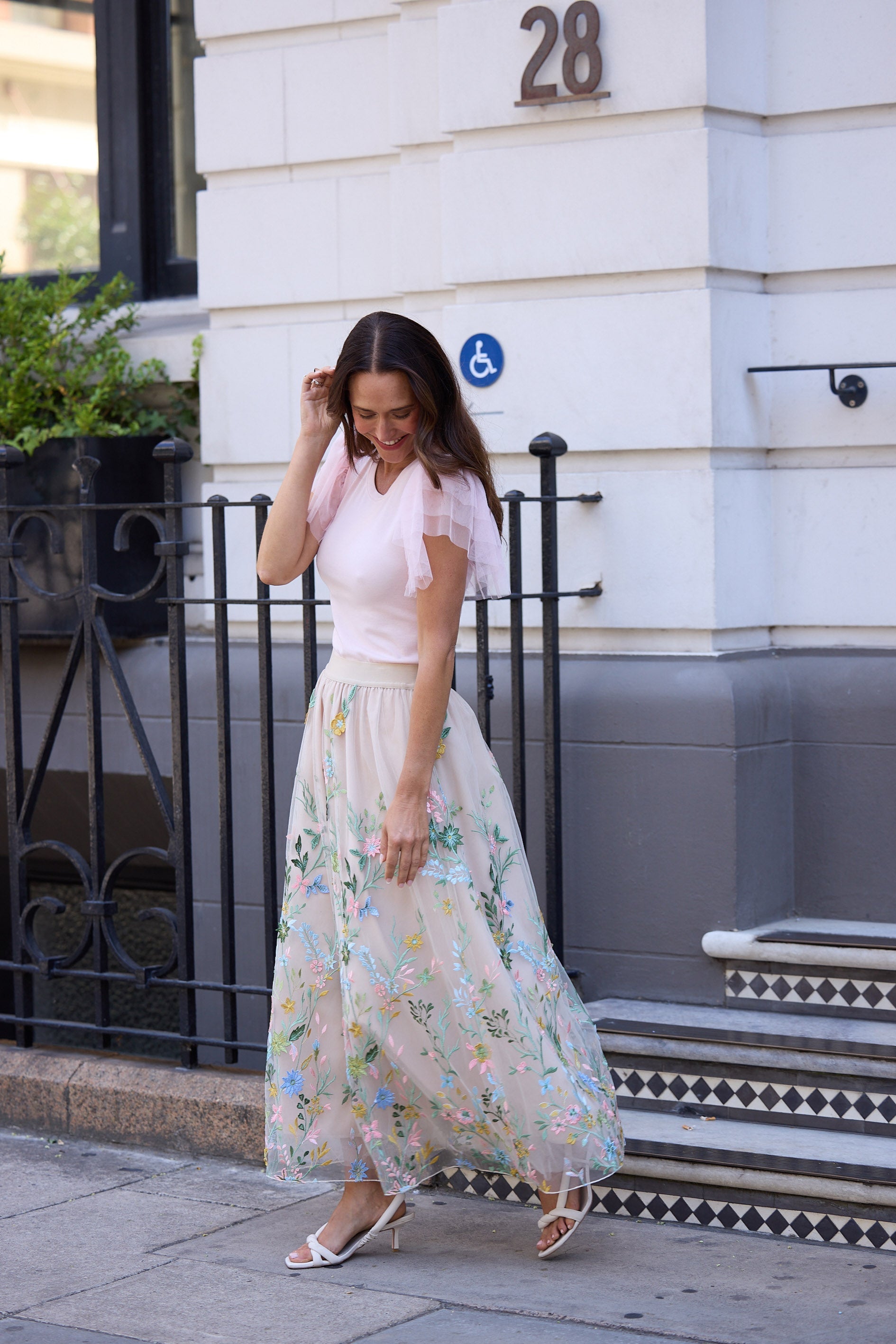 Woman in a floral dress standing in front of a building with number 28