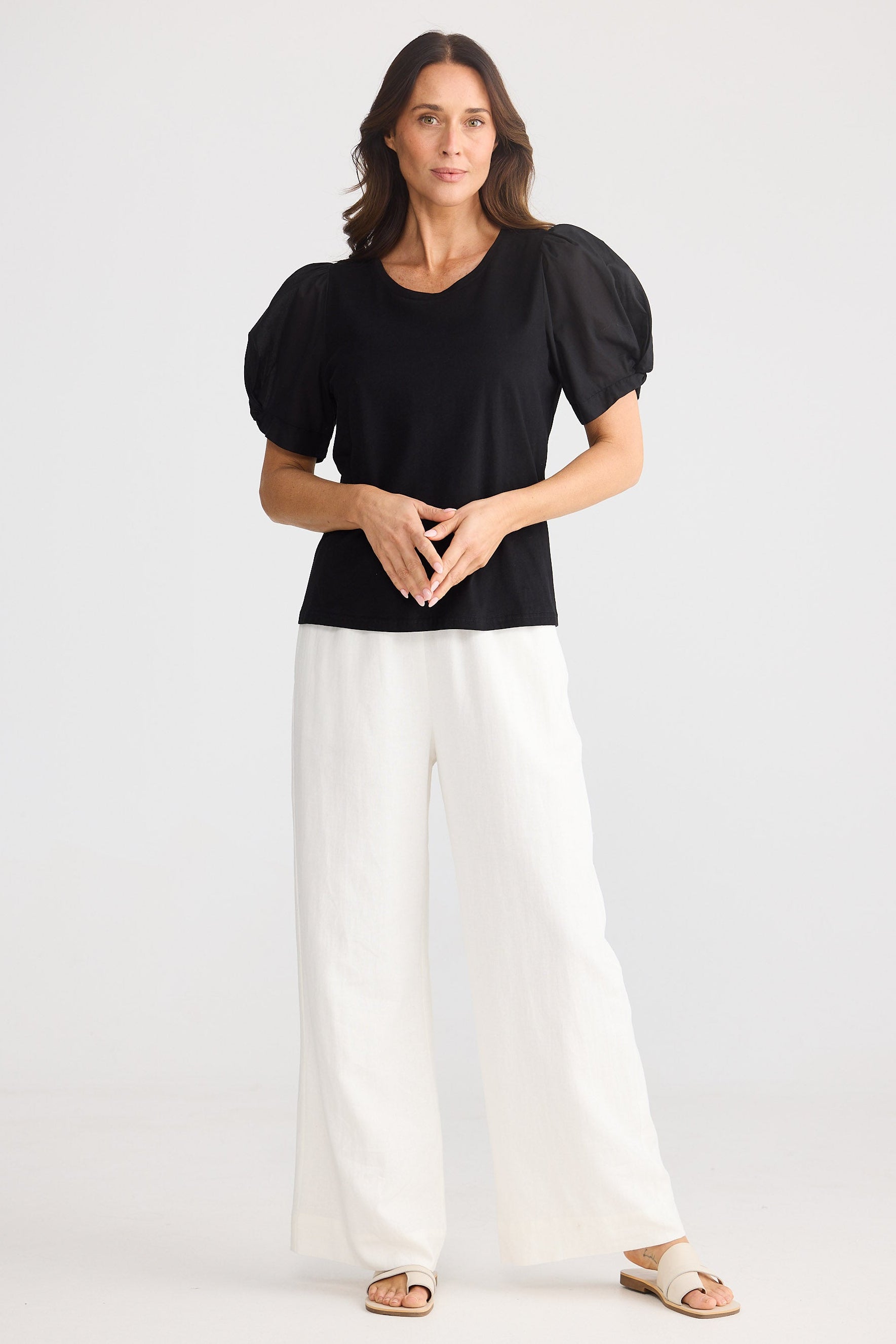 Woman wearing a black top and white pants on a white background