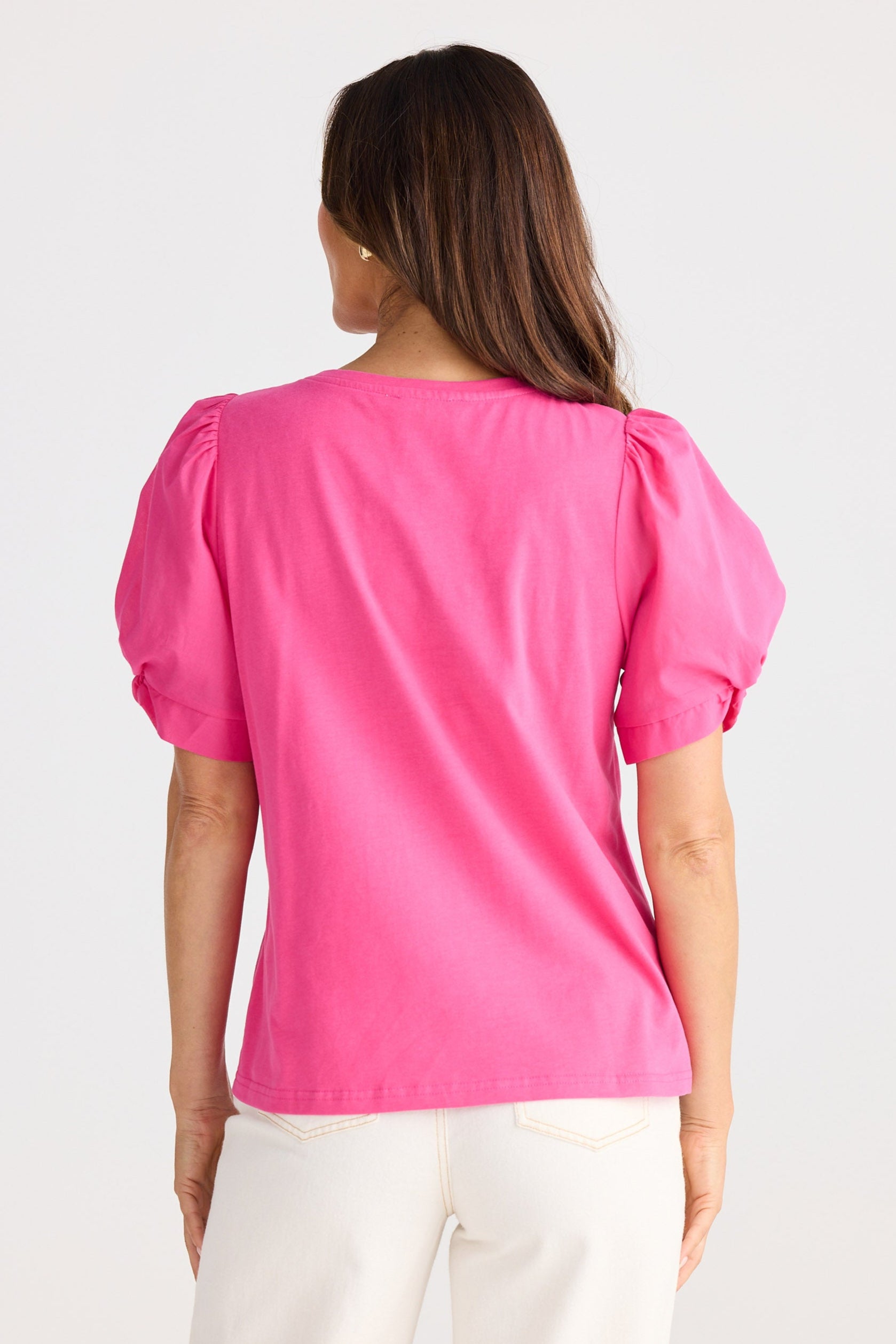 Woman wearing a bright pink blouse with puff sleeves on a white background