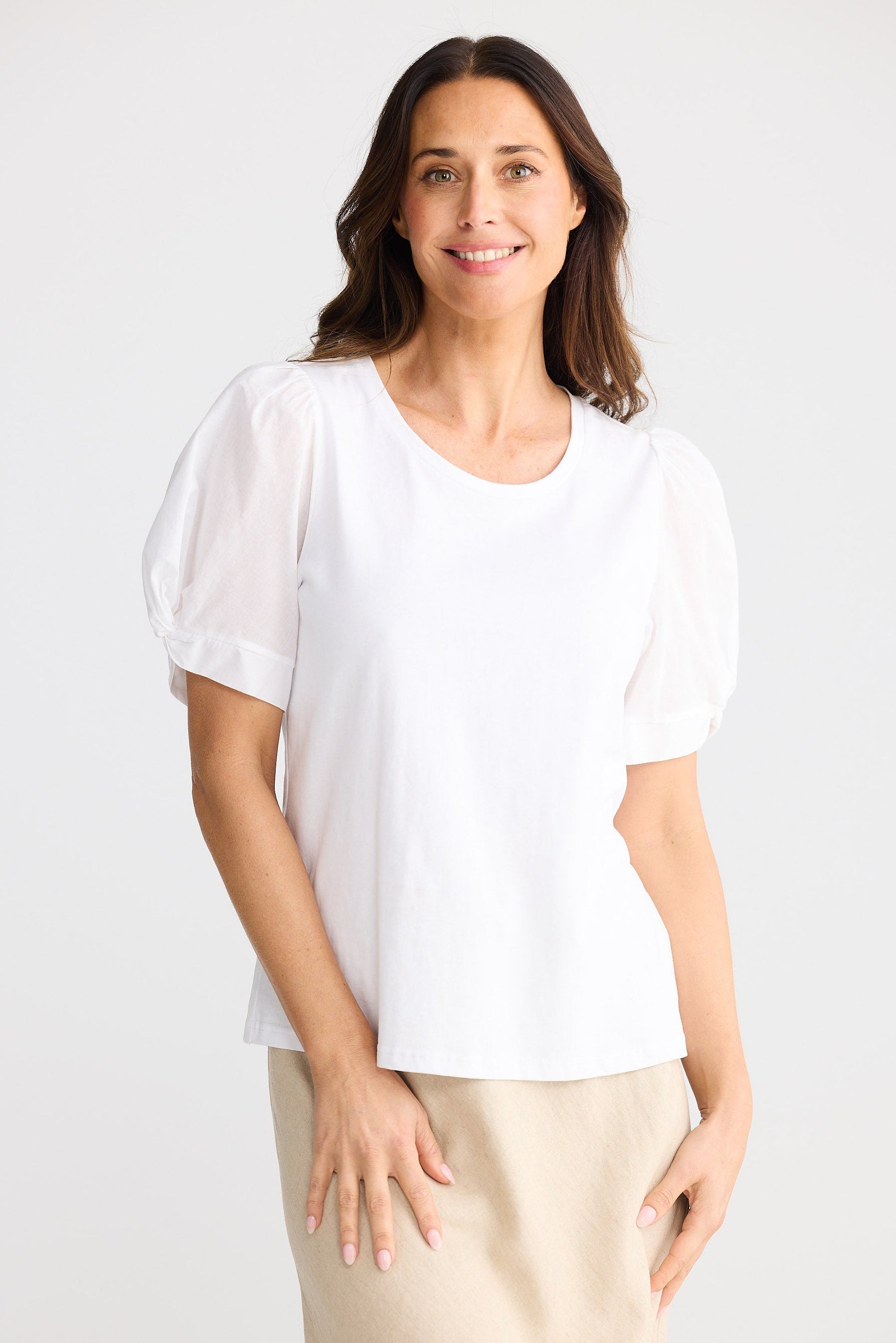 Woman wearing a white blouse and beige pants against a white background