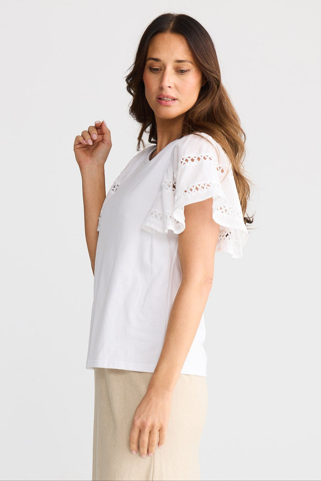 Woman wearing a white blouse with lace sleeves and beige pants on a white background