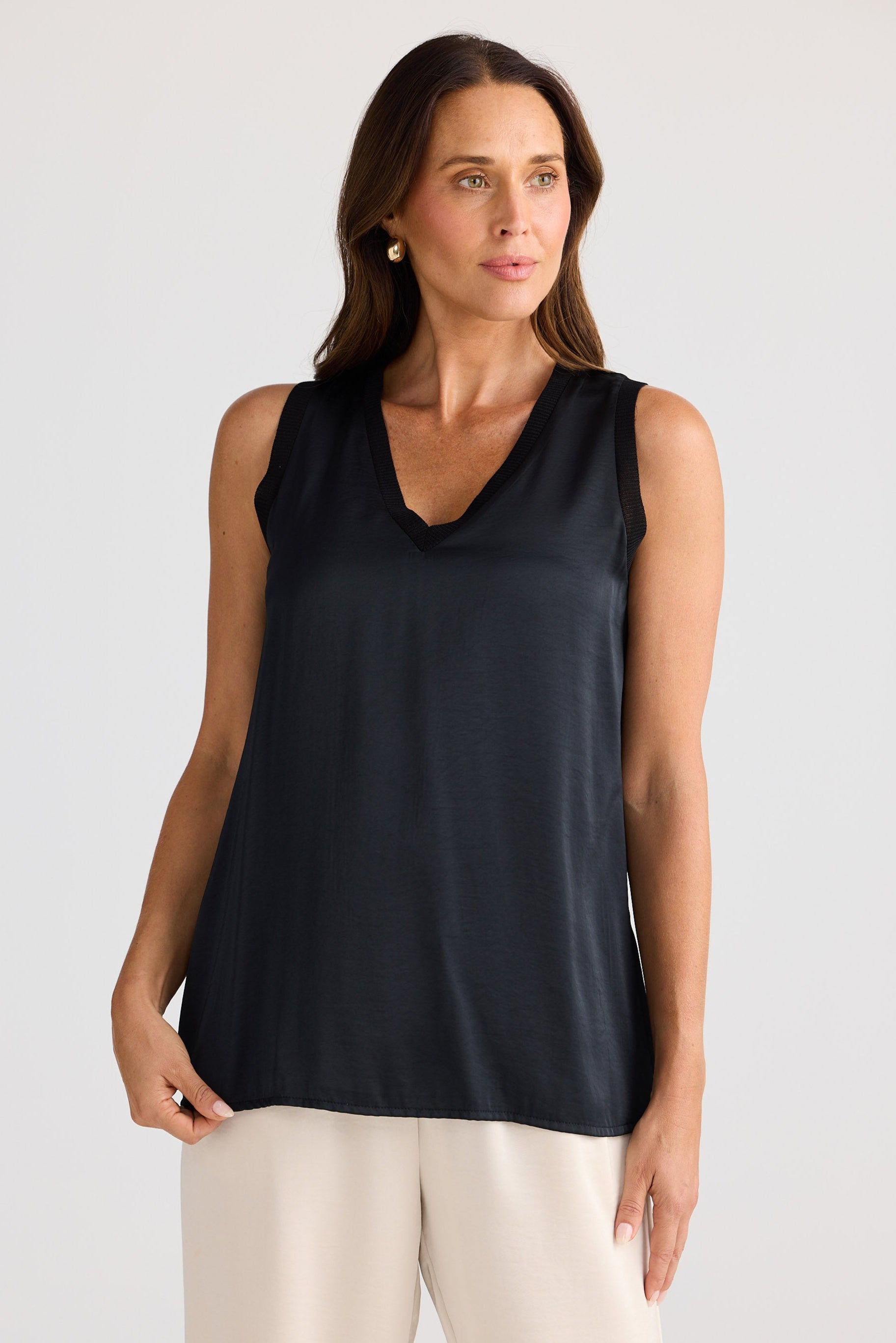 Woman wearing a black sleeveless top and beige pants against a plain background