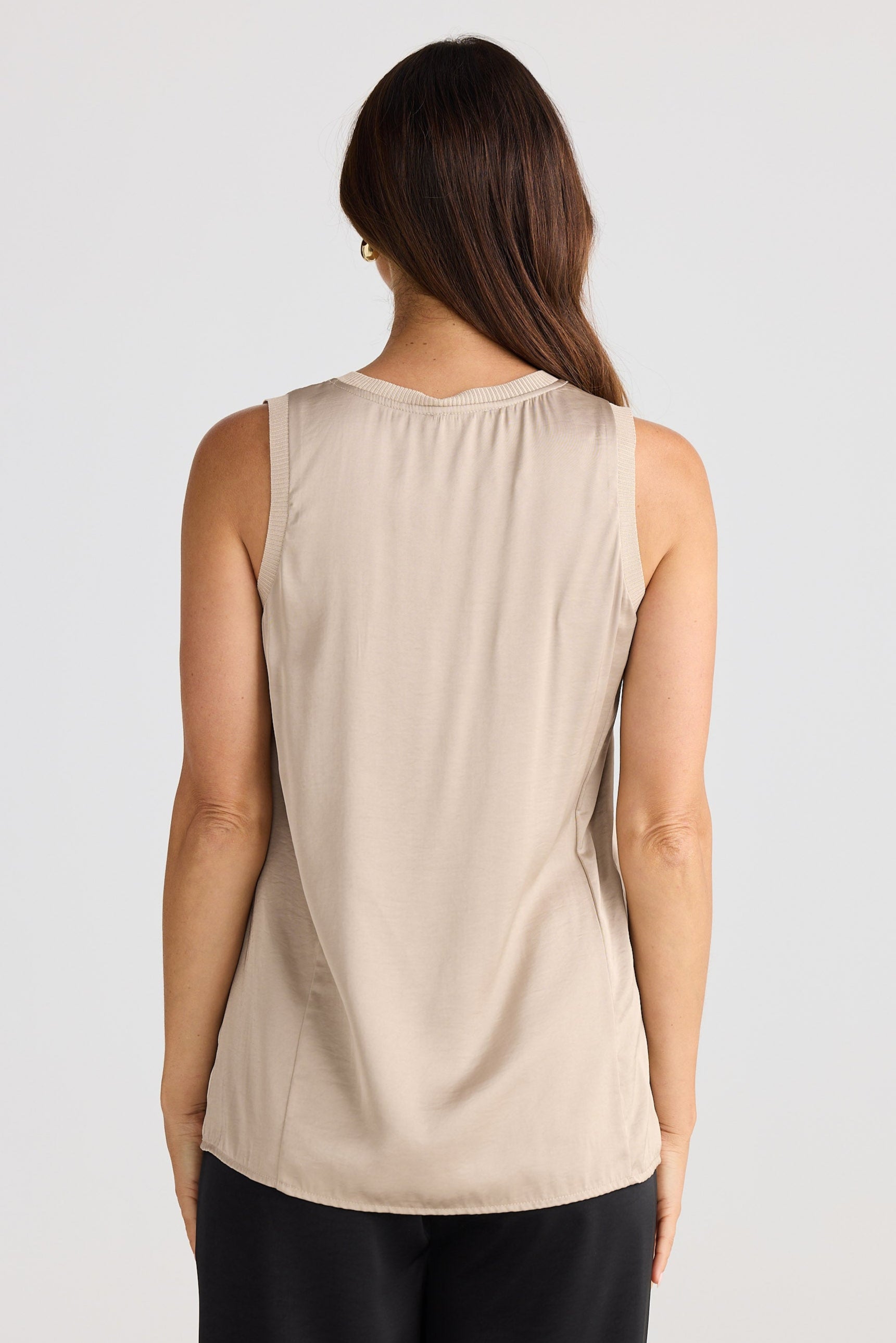 Woman wearing a beige sleeveless top and black pants on a white background