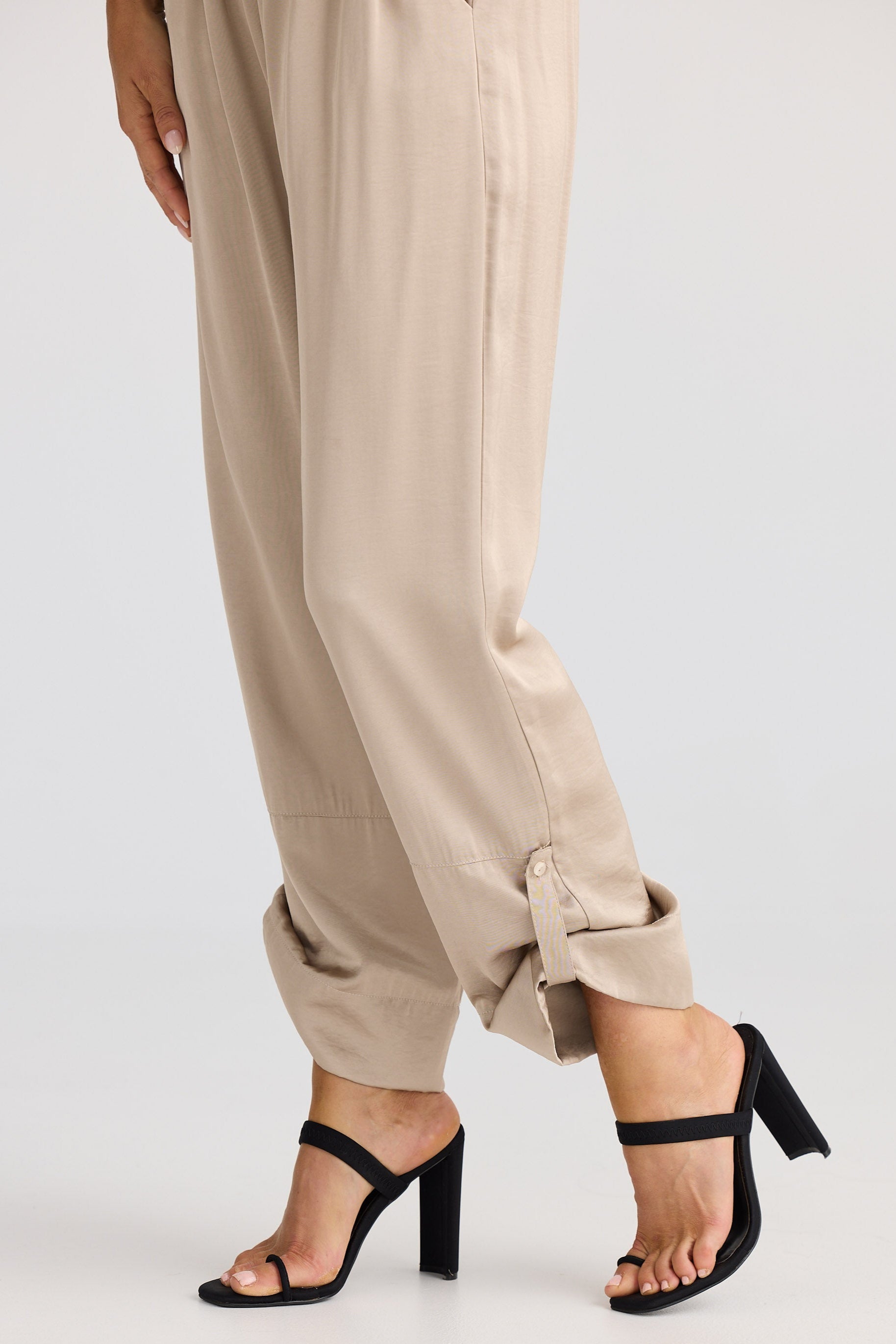 Person wearing beige pants and black high-heeled sandals on a white background