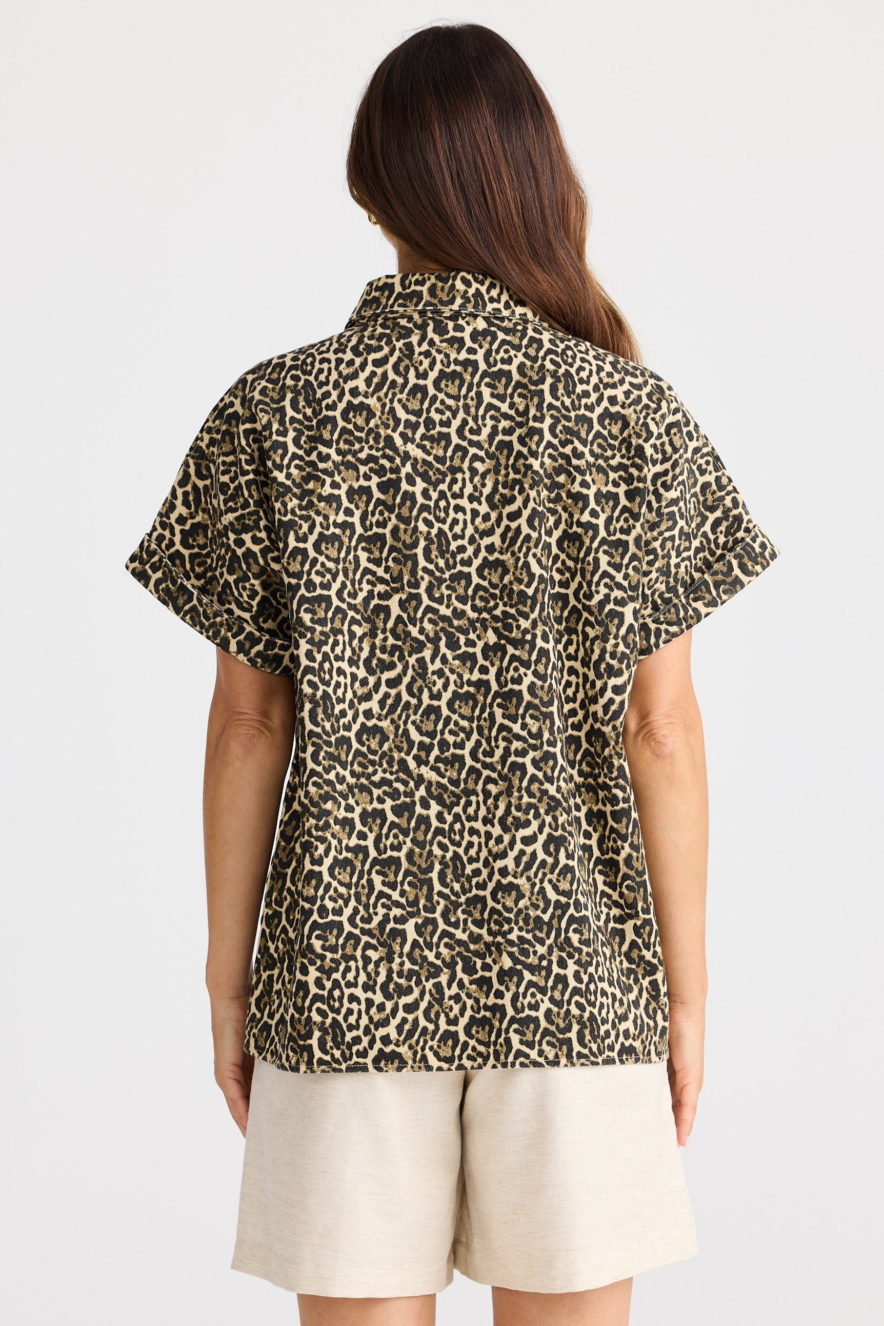 Person wearing a leopard print shirt and beige shorts on a white background