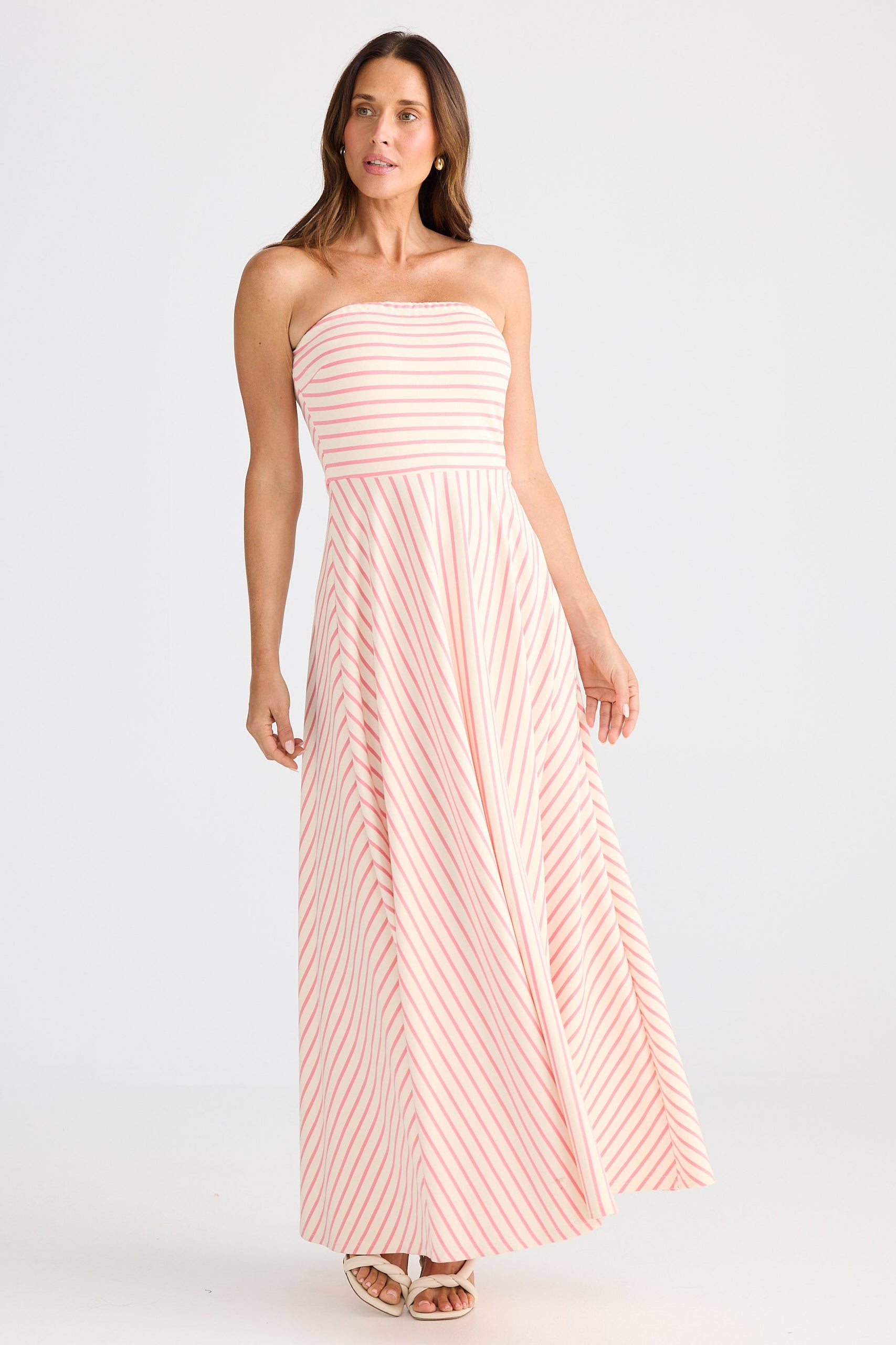 Woman wearing a strapless, long, pink and white striped dress on a white background