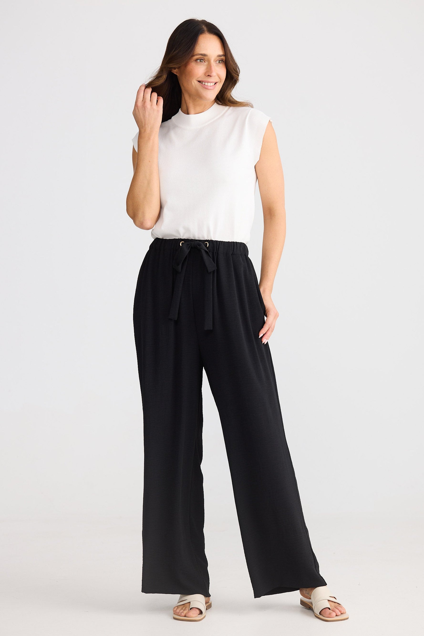 Woman wearing a white sleeveless top and black wide-leg pants on a white background