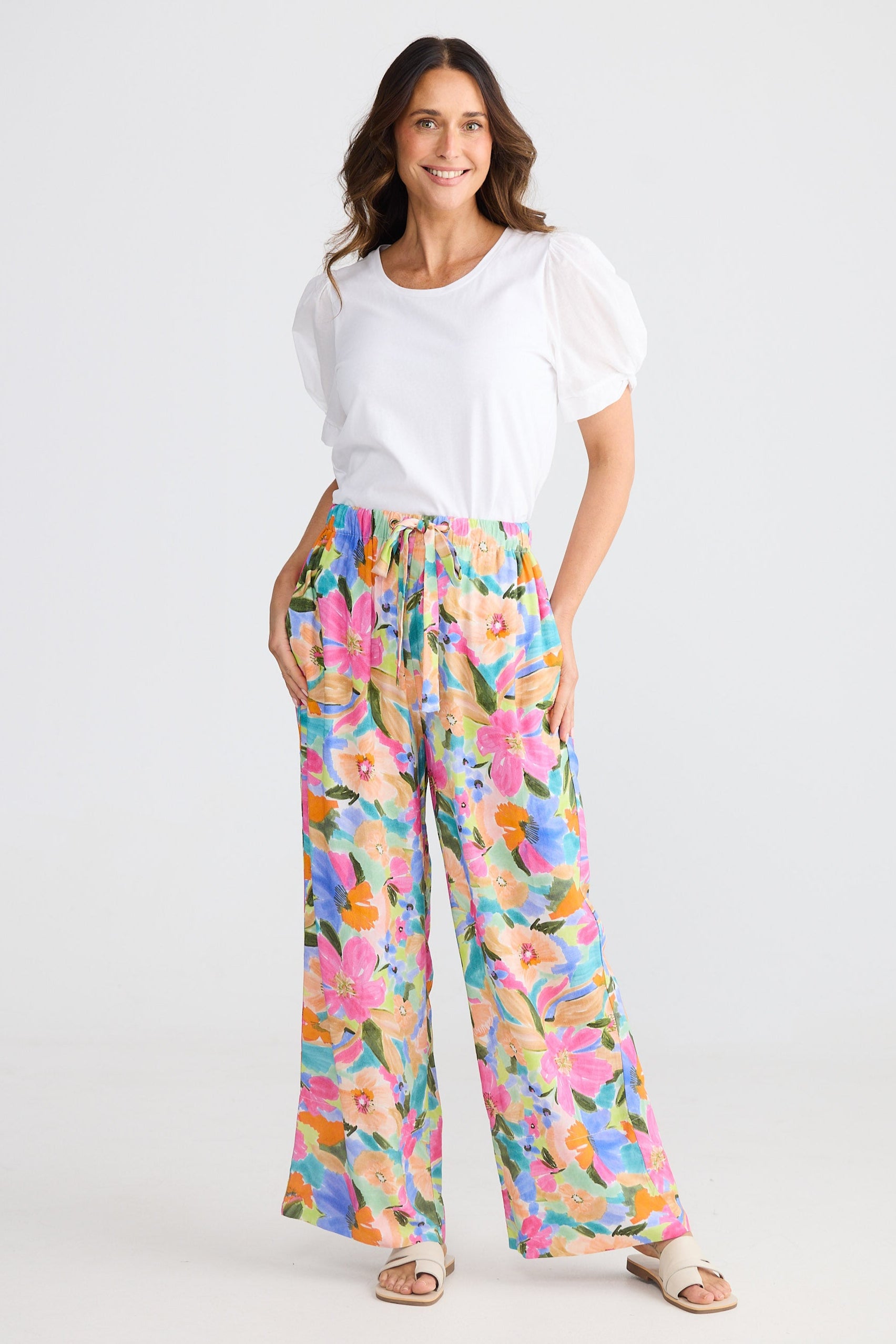 Woman wearing a white top and colorful floral pants on a white background