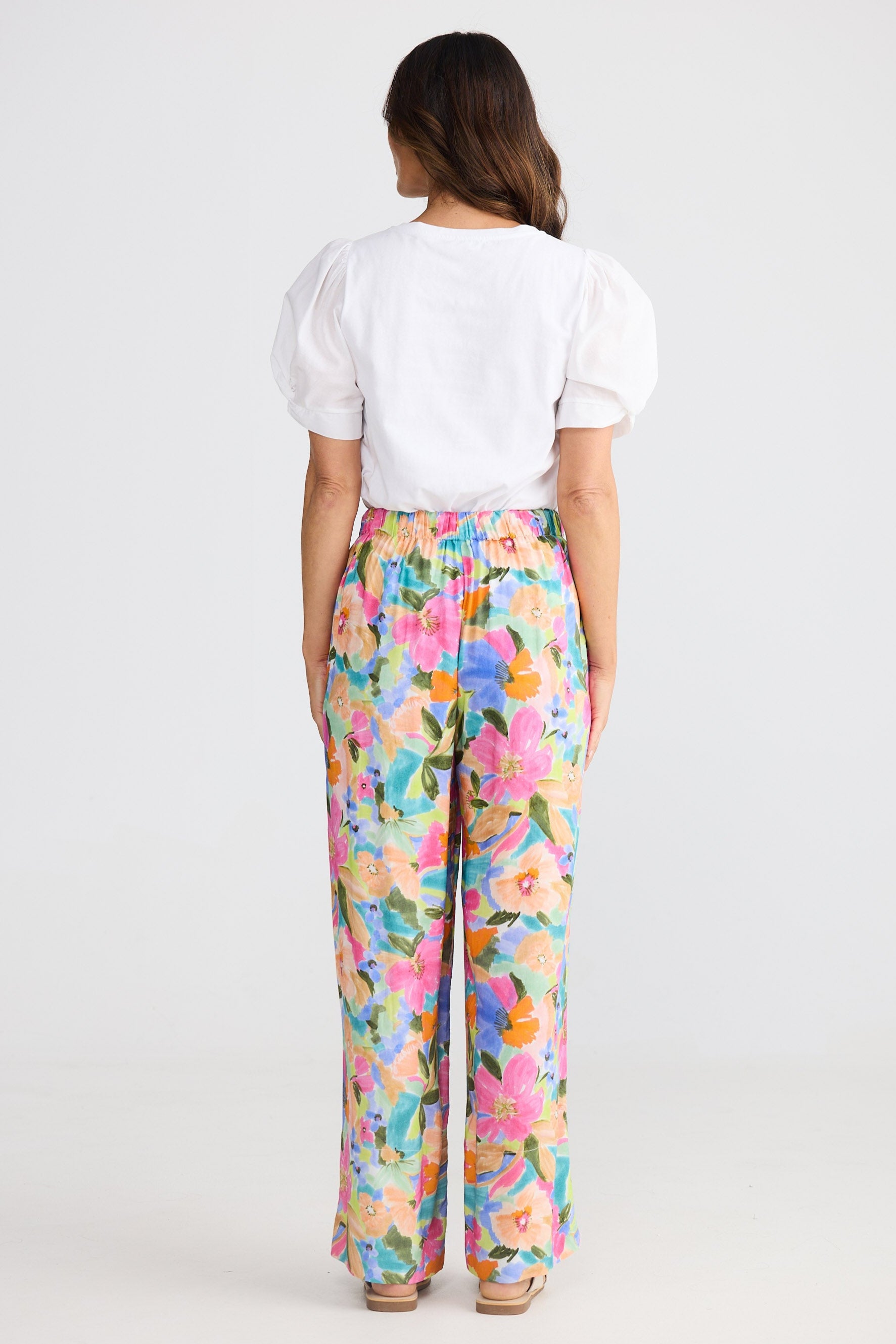 Person wearing a white top and colorful floral pants on a white background